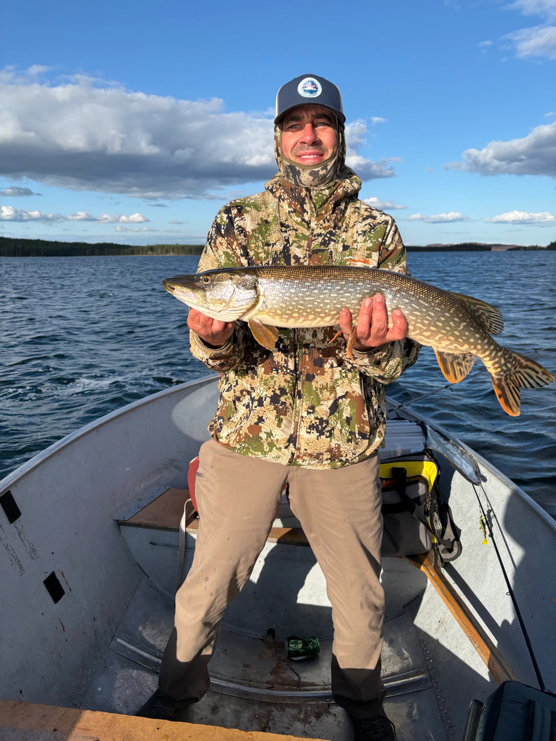 Person on boat holding large fish with lake and sky in background.