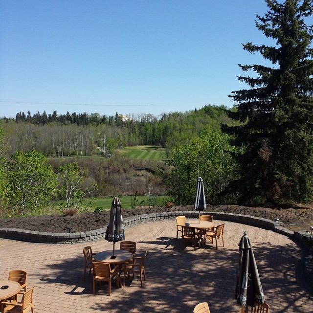 Outdoor patio with wooden tables, umbrellas, and scenic greenery.