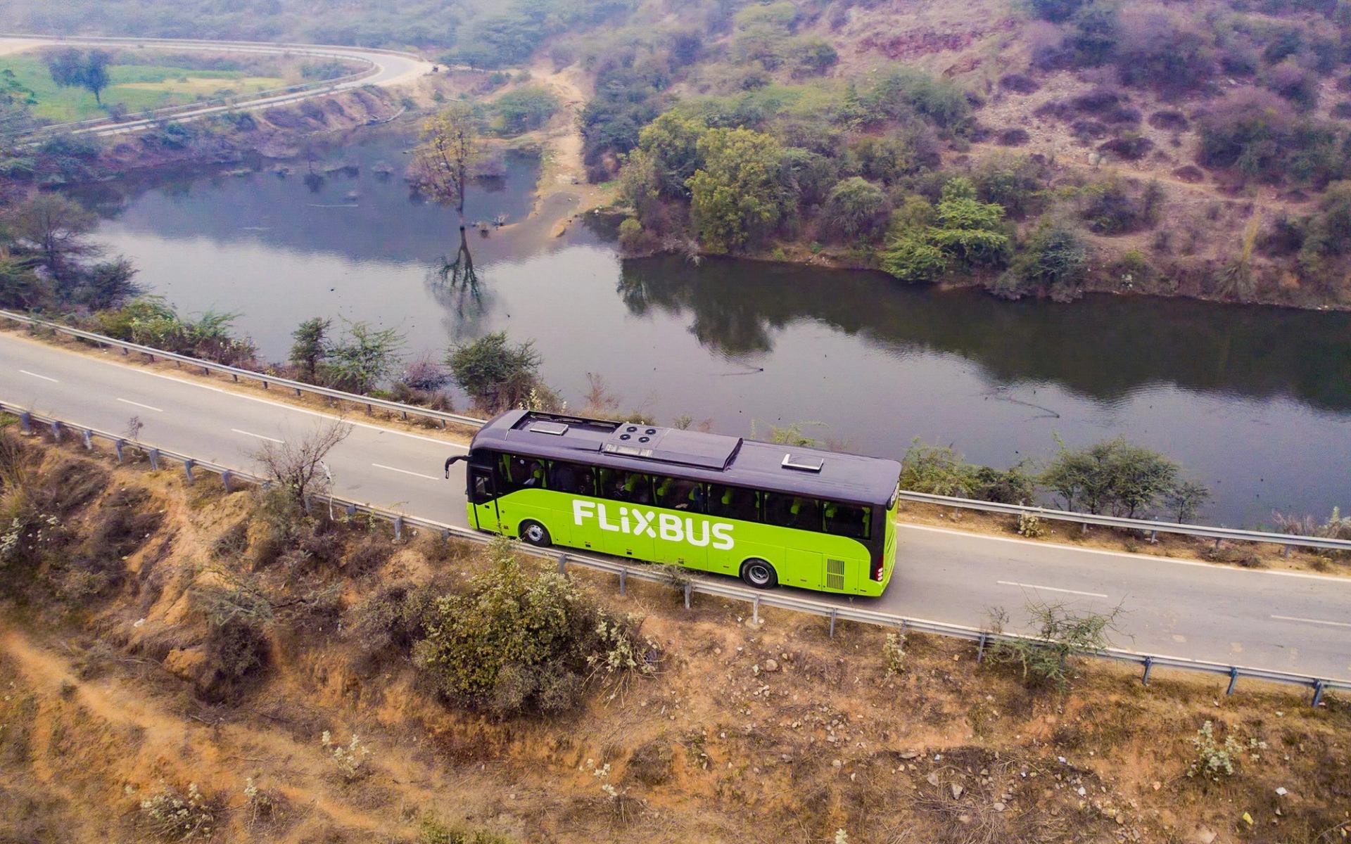 An overhead photo of a bus as it travels on a road with a body of water in the background.