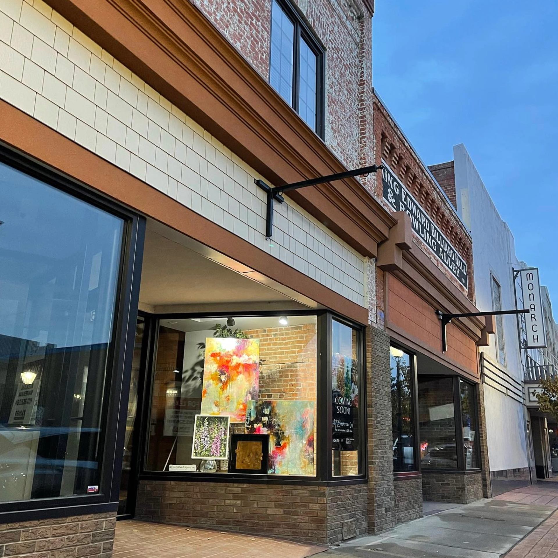 Art gallery storefront with large windows displaying colourful abstract paintings and street reflections.