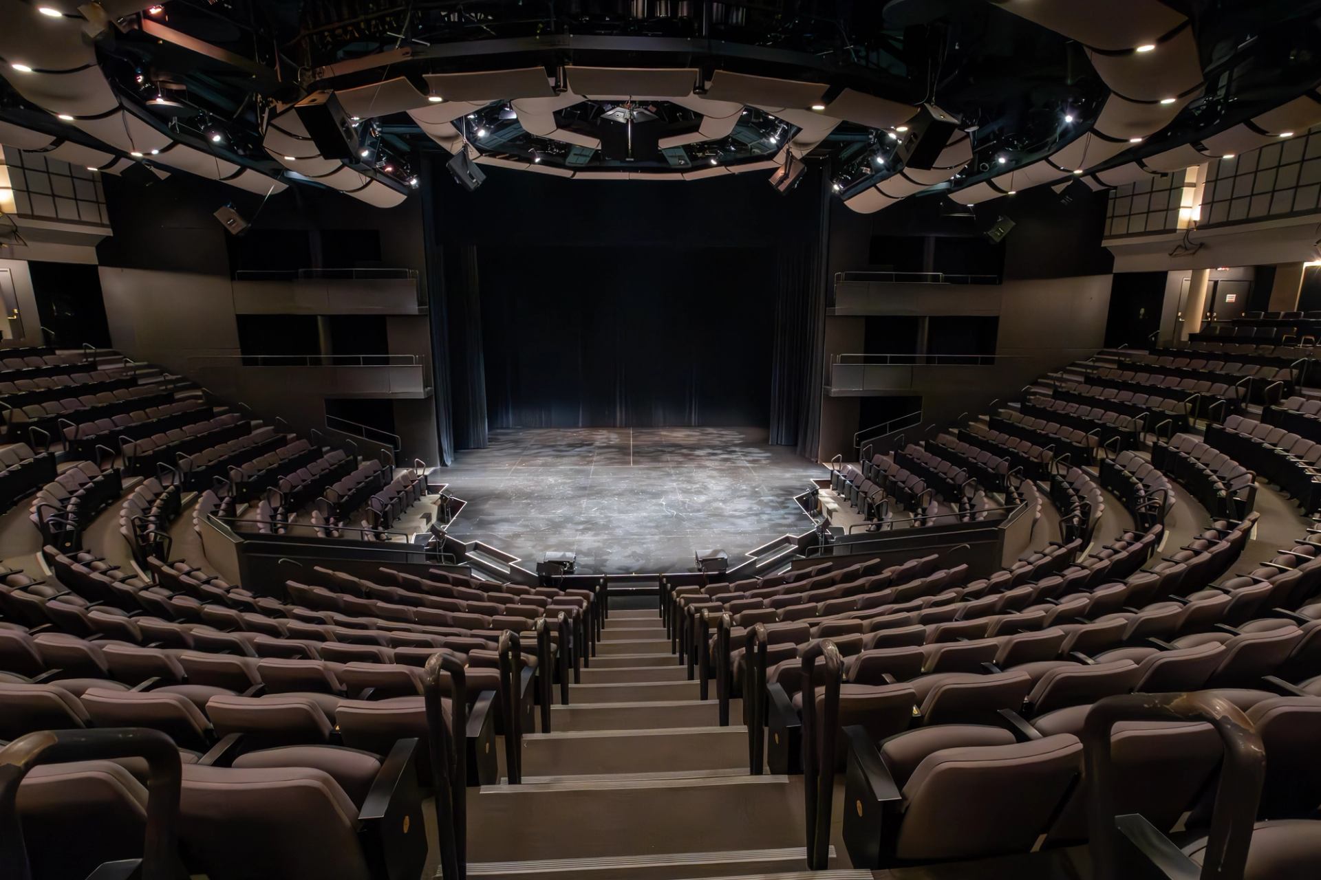 Empty theatre auditorium with curved seating facing a black-curtained stage.