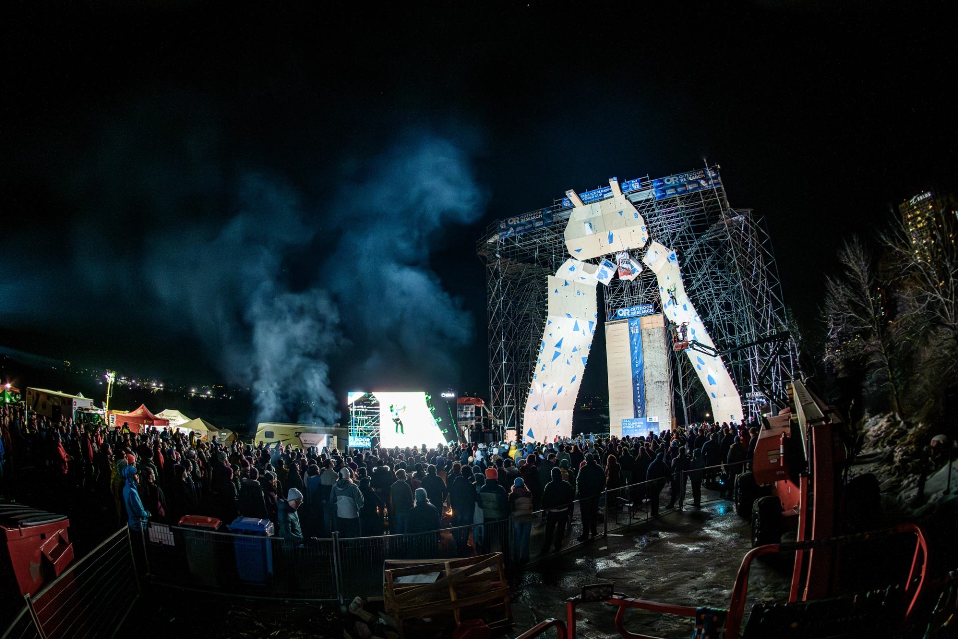 Night crowd watching climbers on illuminated ice wall at UIAA Ice Climbing World Cup.