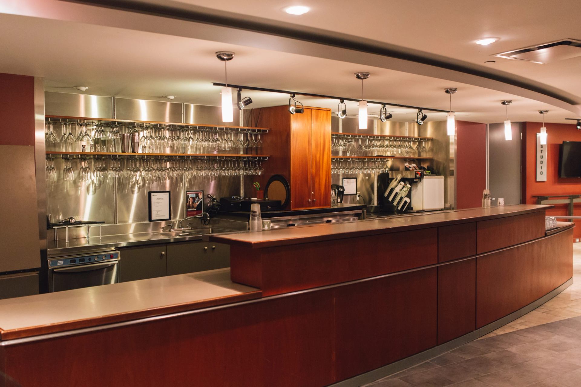 Modern bar counter with hanging glassware, stainless steel backsplash and warm pendant lights.