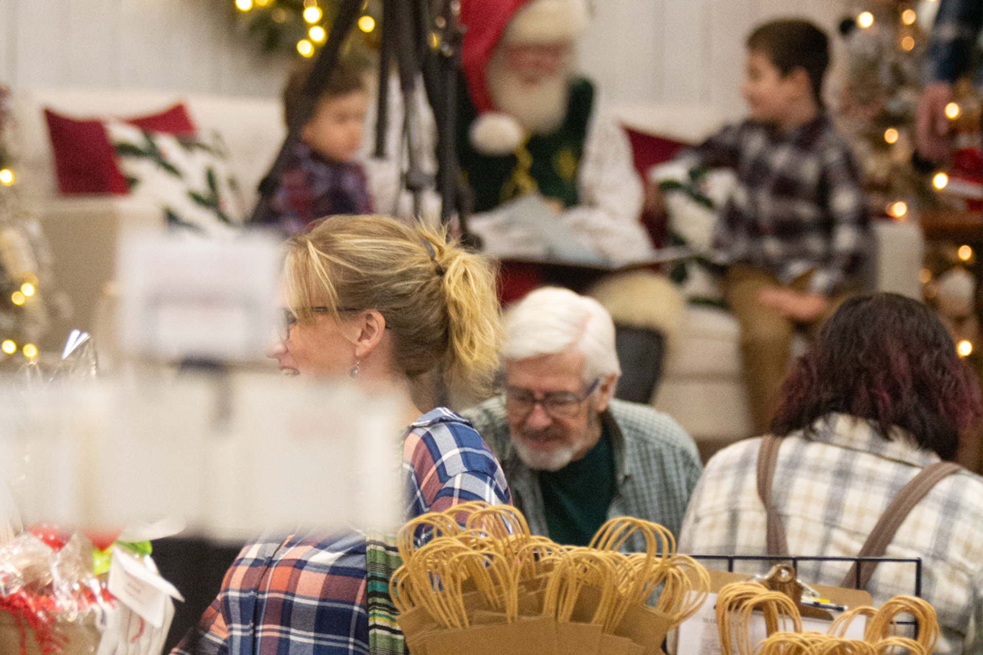 Santa Claus seated indoors with children and festive decorations in a holiday-themed setting.