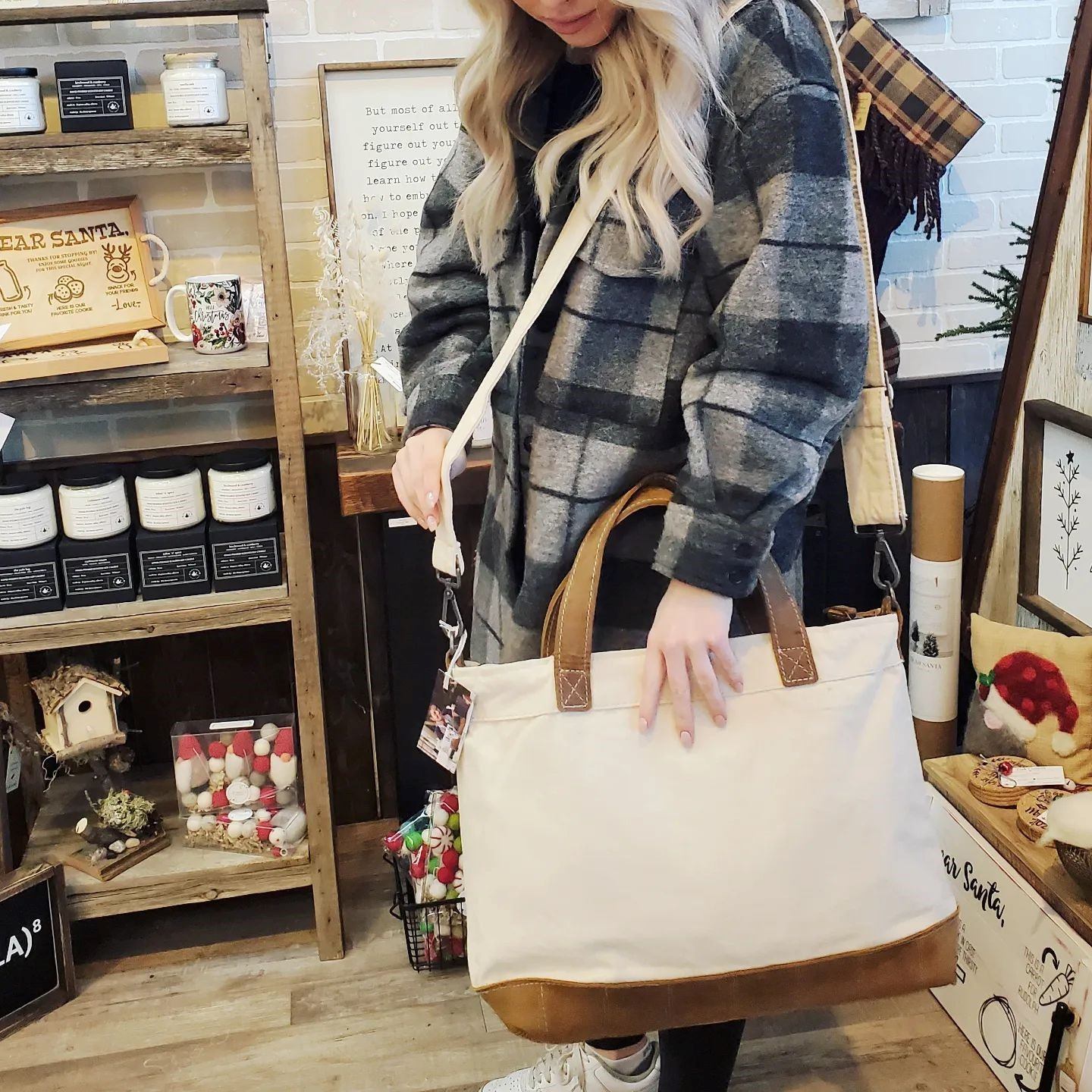 Person holding beige tote bag in store with shelves of candles and decor items.