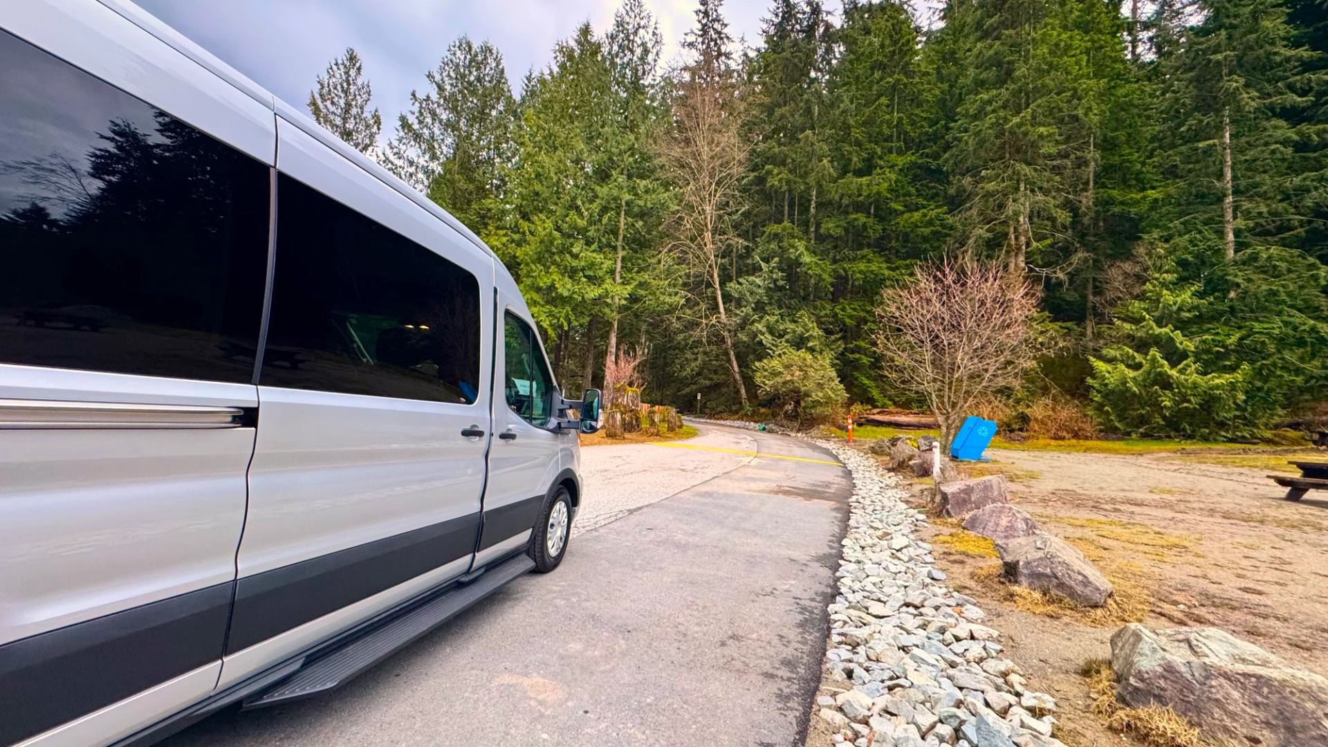 White van parked beside curved road near forested area and picnic site.