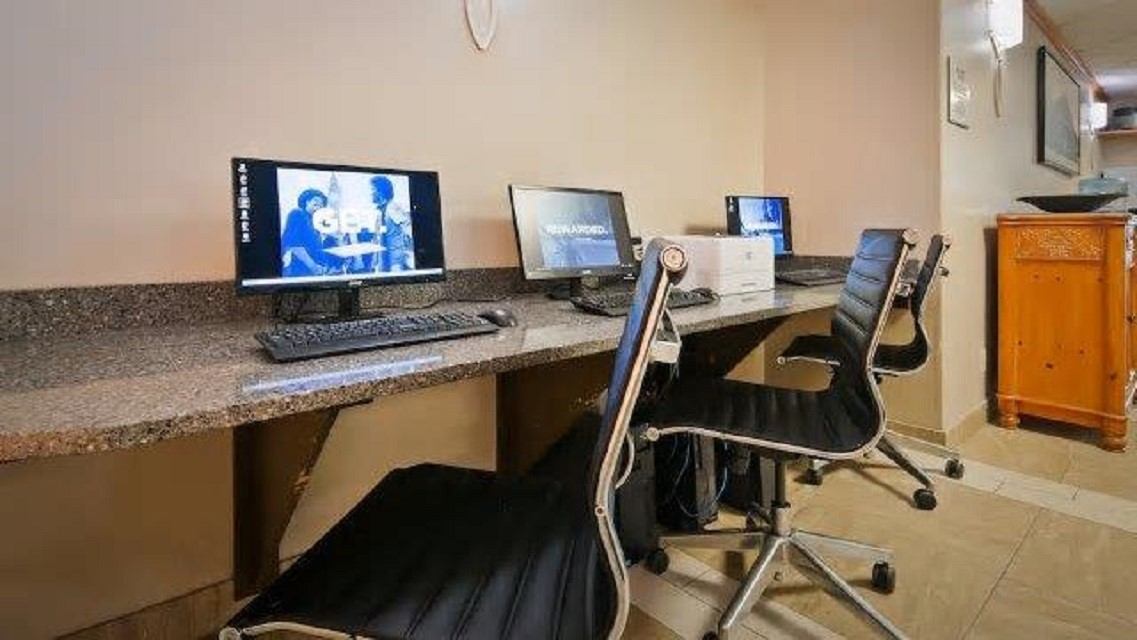 Office reception desk with two monitors, computer screens, and swivel chairs in a hotel room.