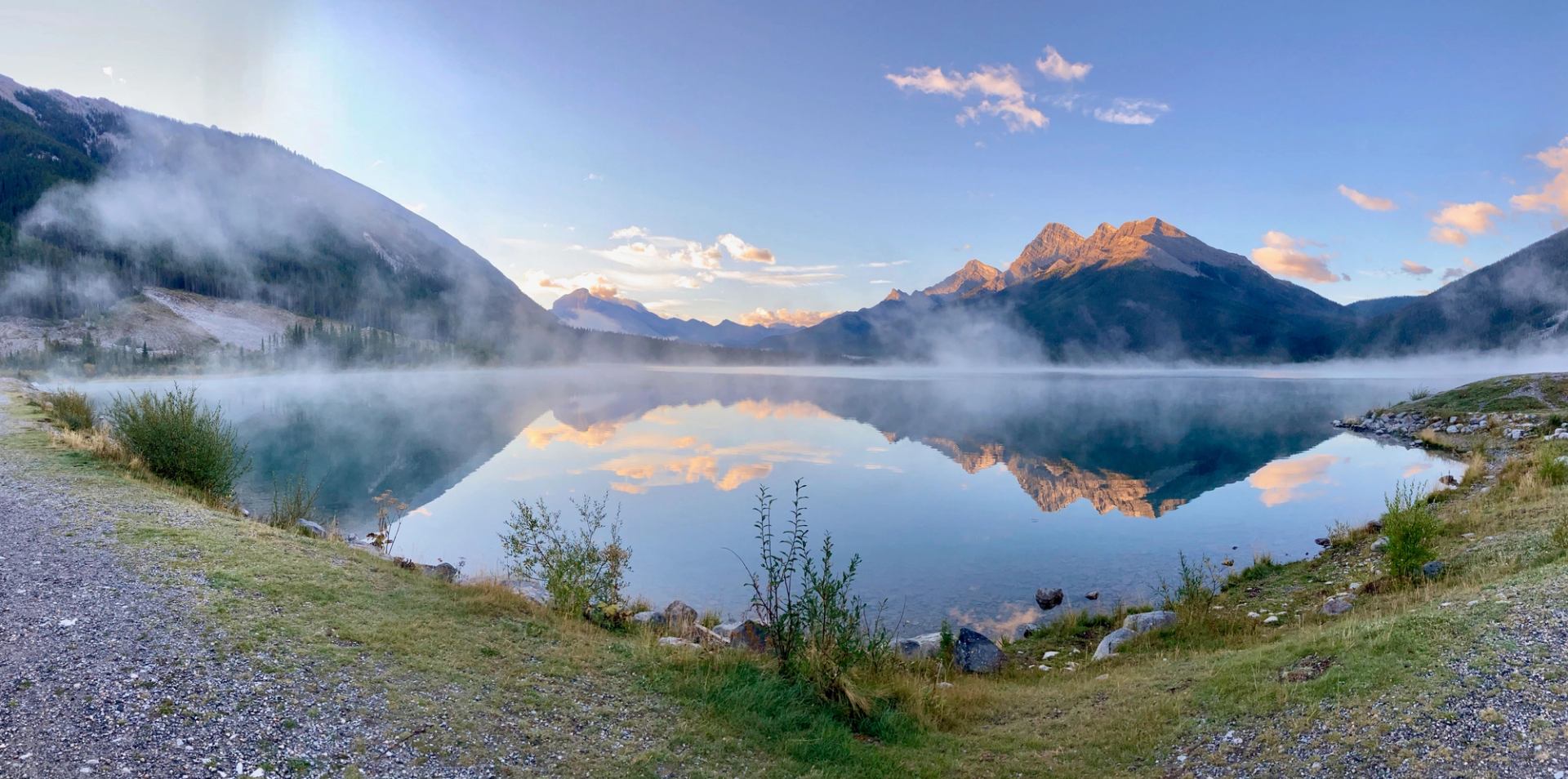 Calm mountain lake with mist rising, reflecting peaks and clouds in Bow Valley.