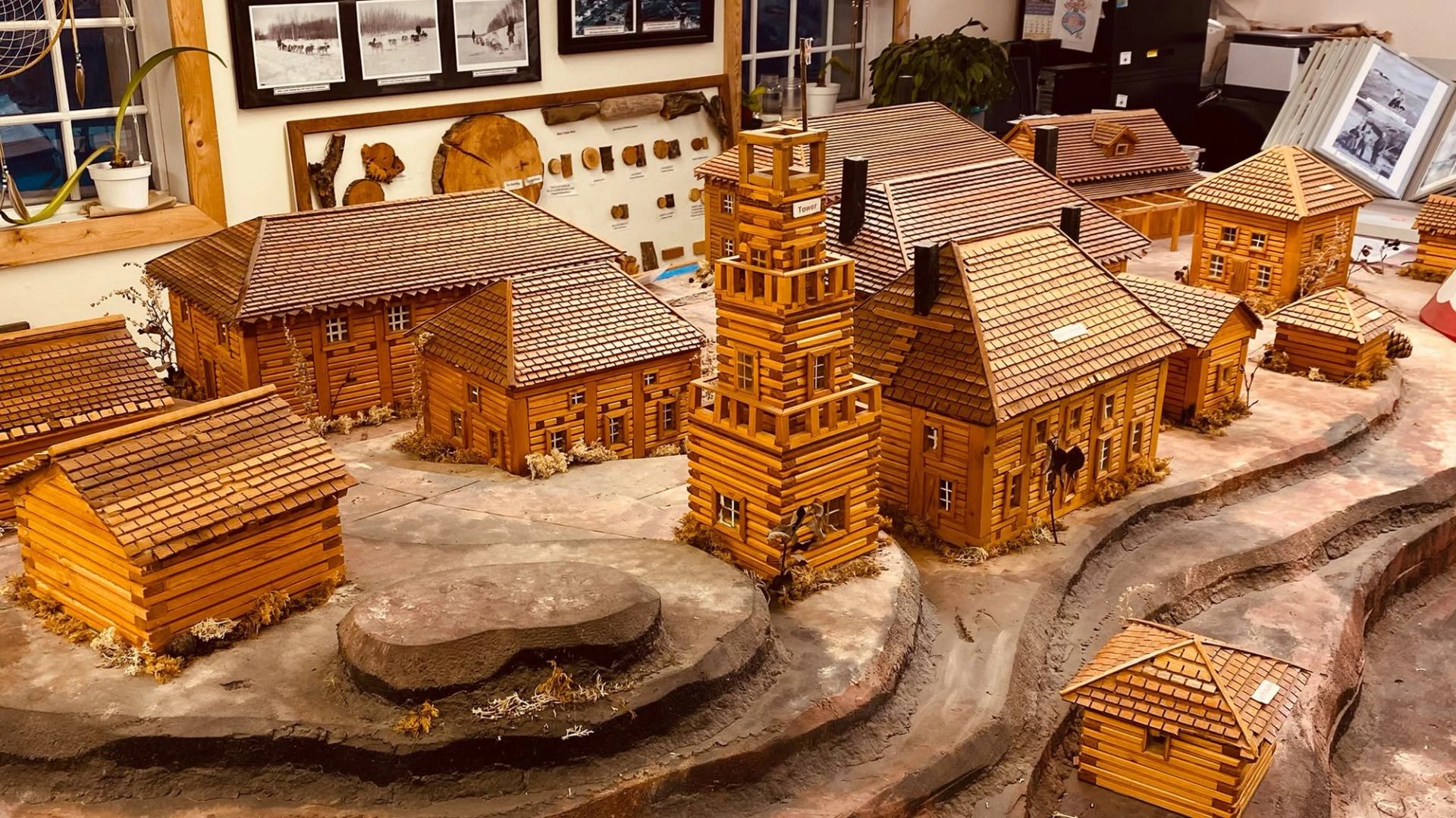 Detailed wooden model village features log buildings, a central tower and winding roads.