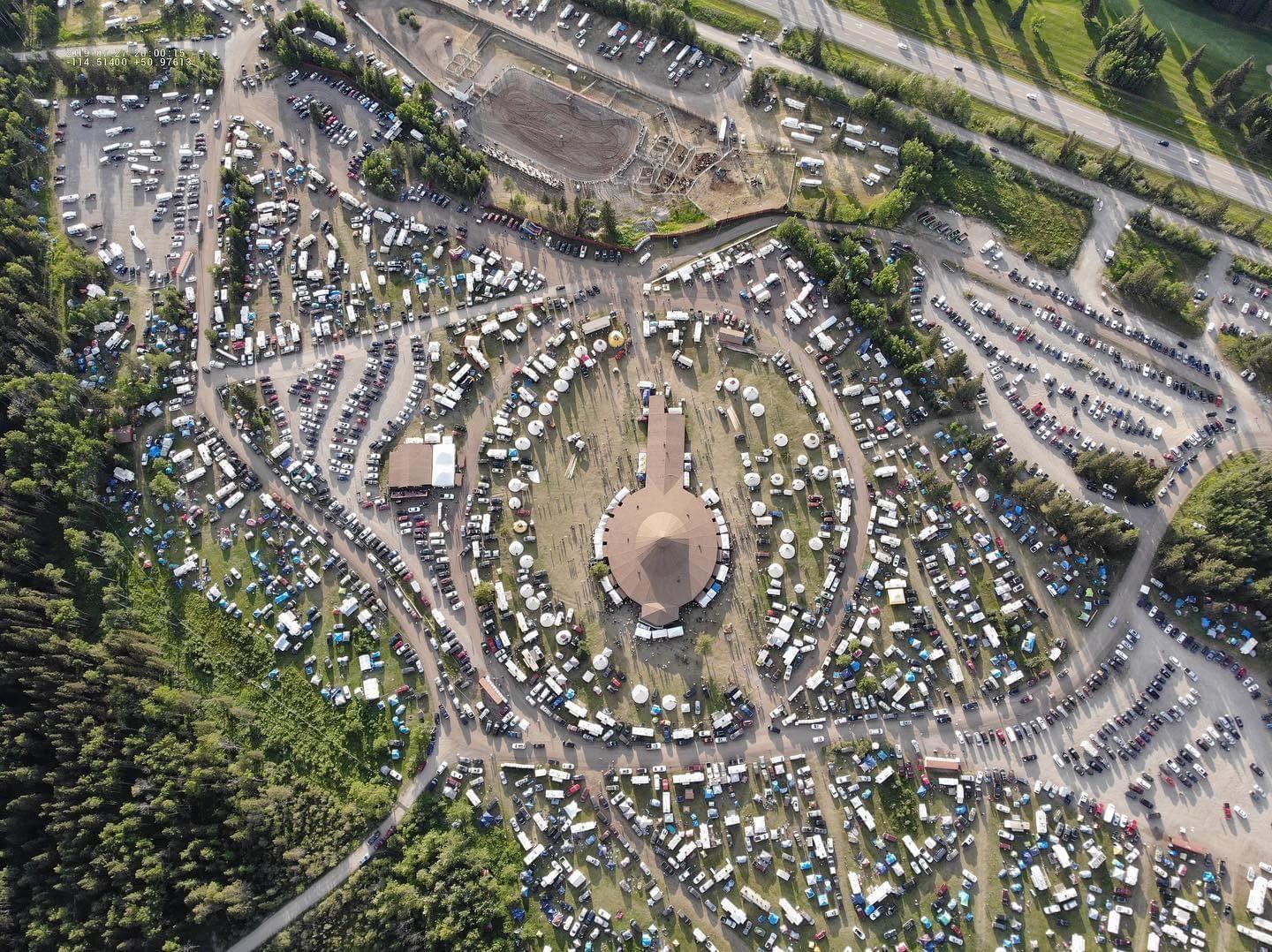 Aerial view of circular campground with RVs, tents and vehicles surrounded by forest.