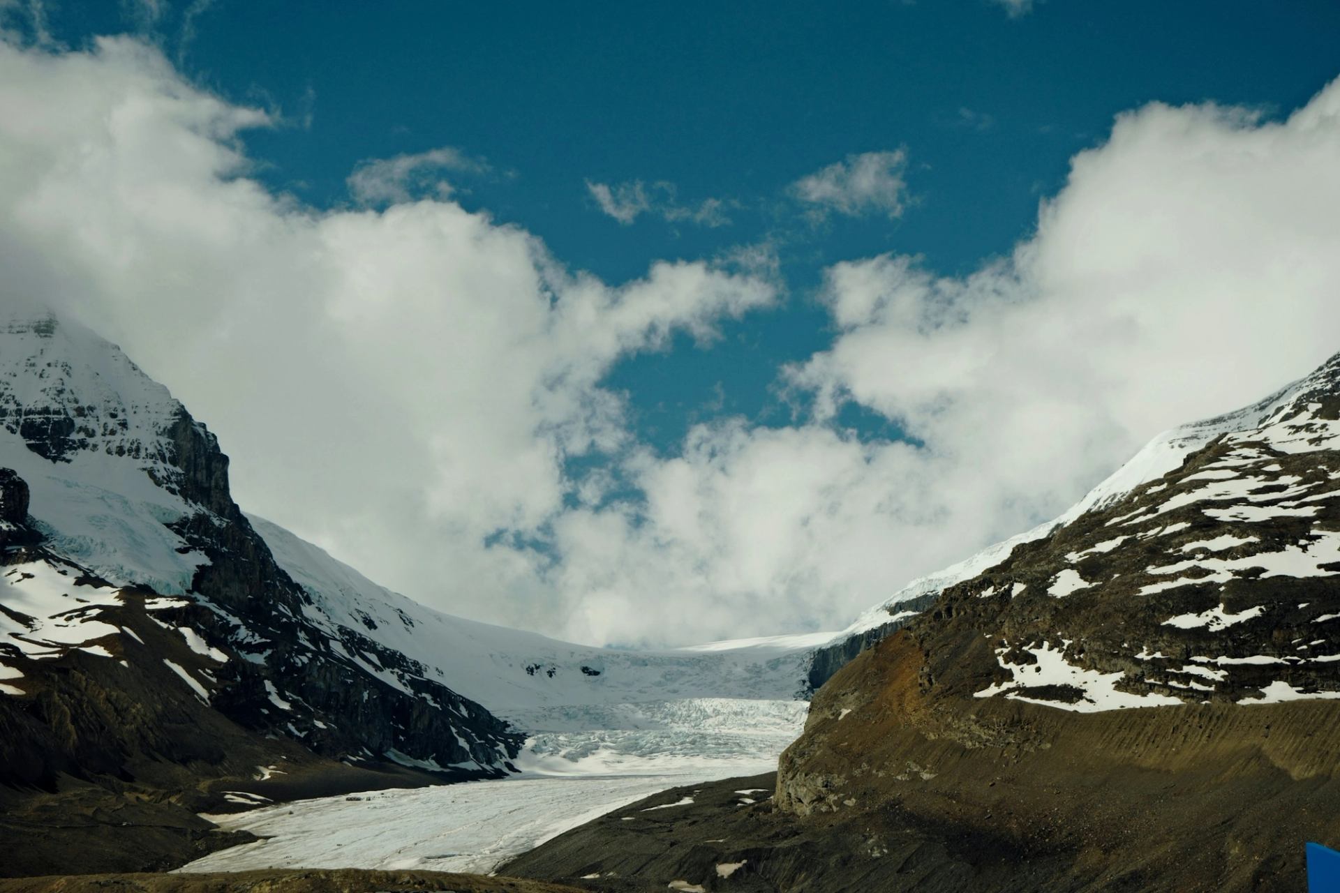 Snow-covered mountain glacier between rocky slopes under a blue sky with scattered clouds.