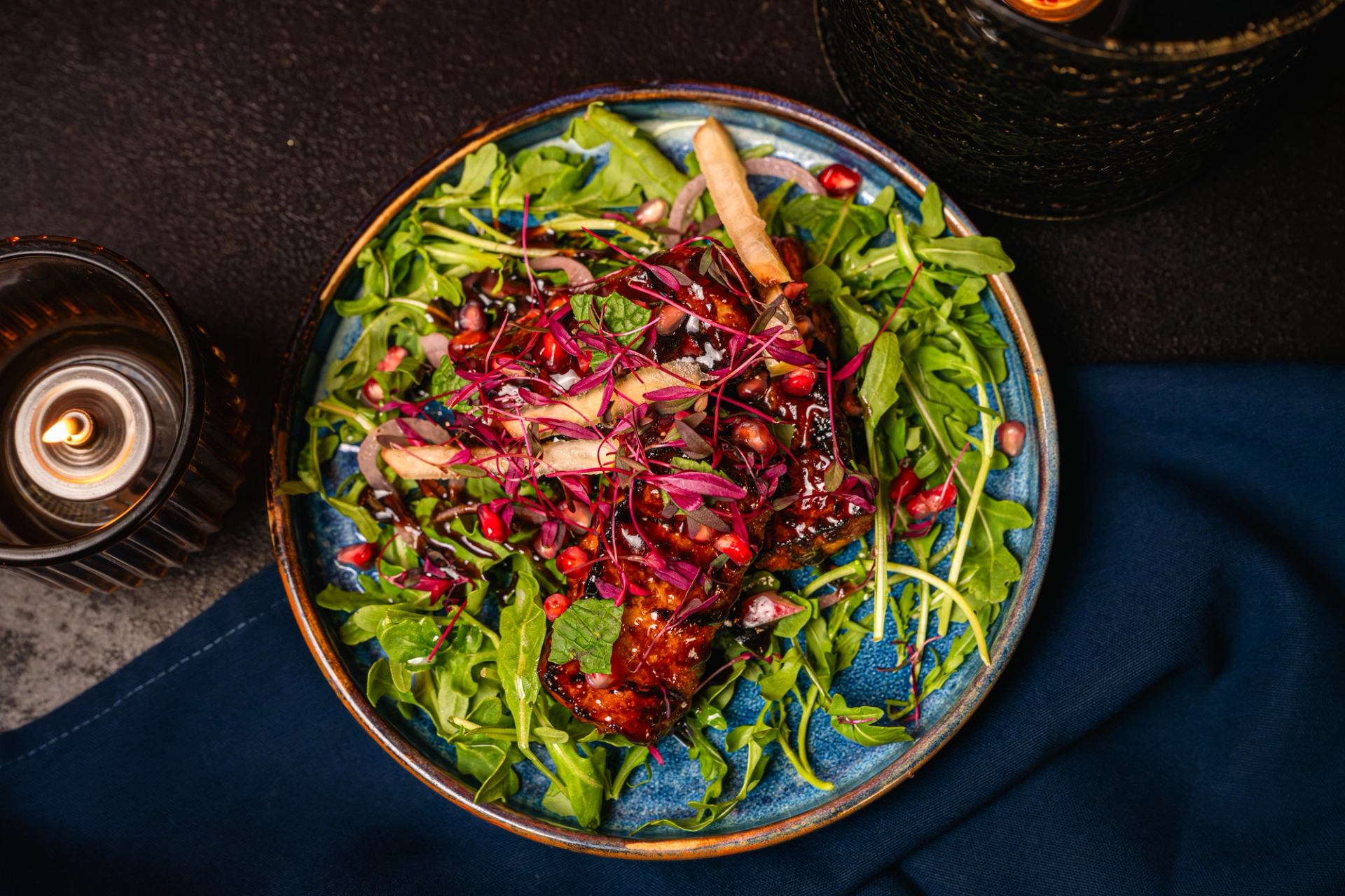Plate of glazed meat on arugula salad with pomegranate seeds and microgreens.