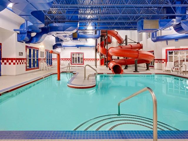 Indoor pool at Ramada Stettler with red and blue slides, fountain, and checkered wall tiles.