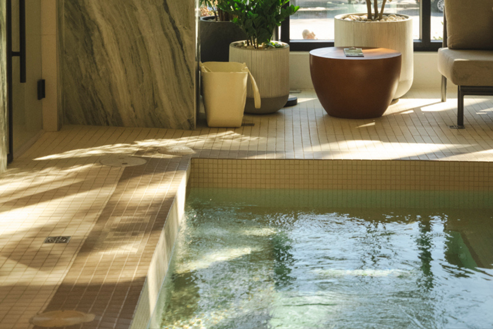 Indoor spa area with a bubbling pool, tiled floor, potted plants, and a marble wall.