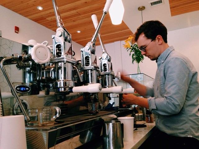 Barista working a lever espresso machine in a bright café.