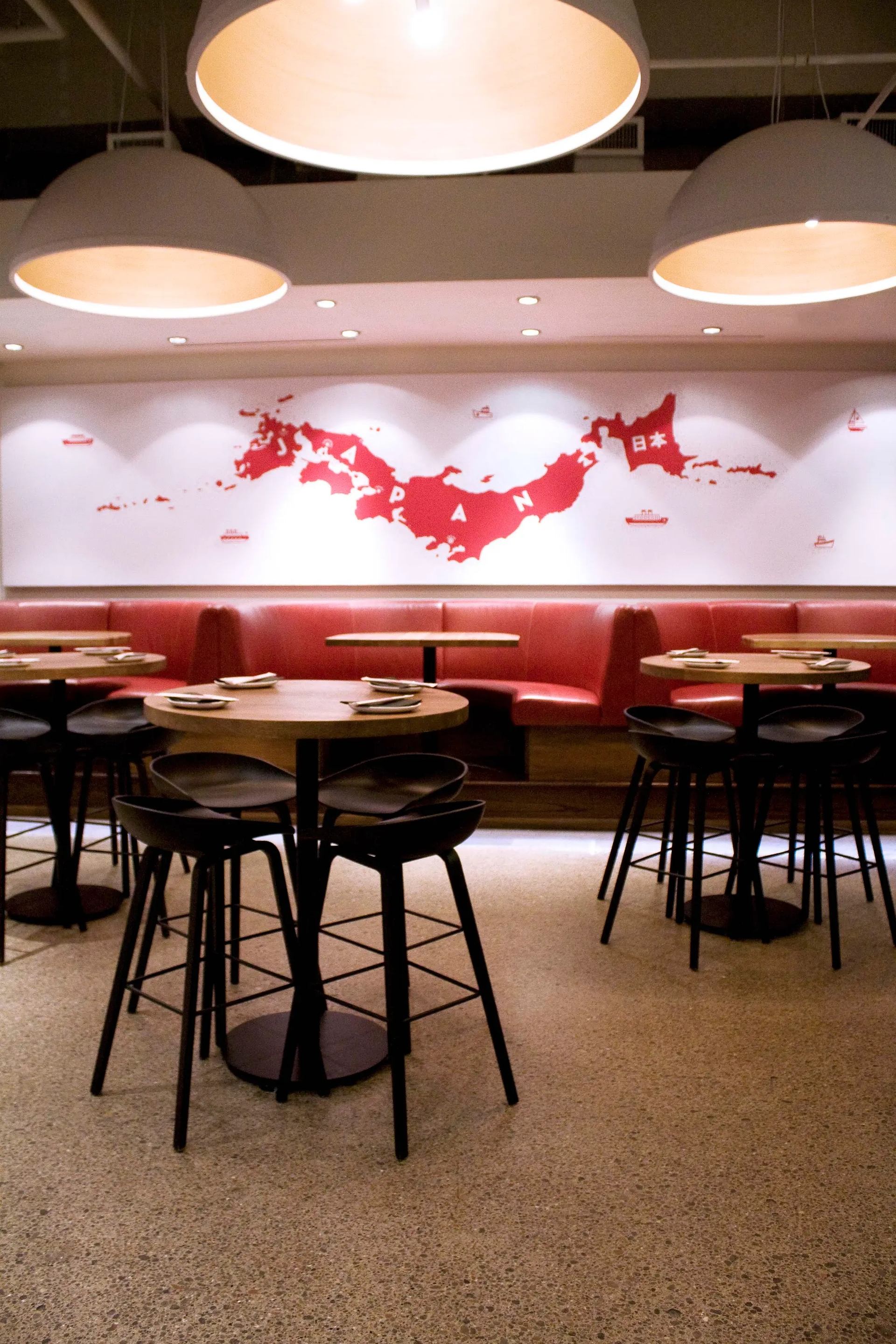 Modern restaurant interior with round tables, stools, and red map wall art.