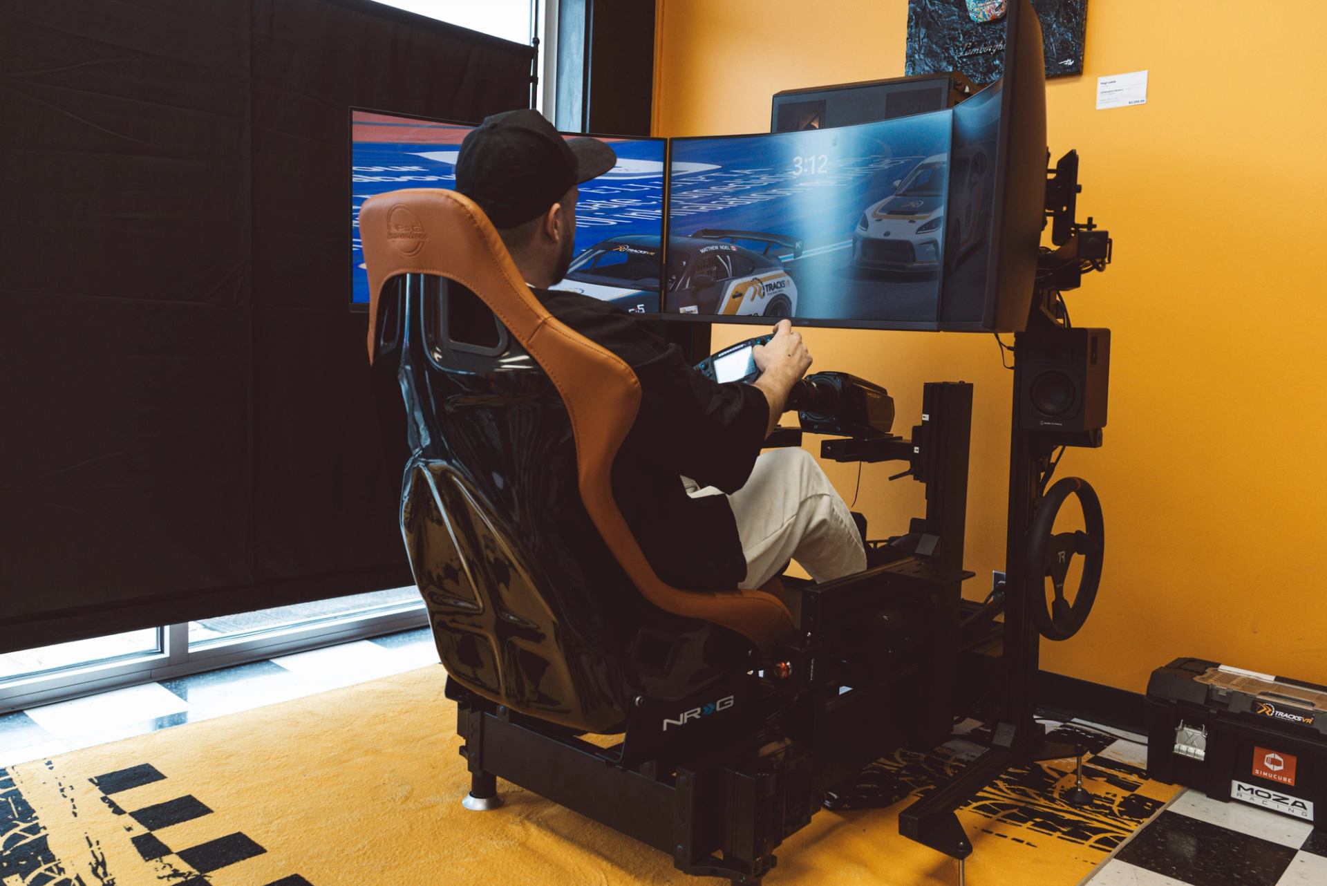 Person in racing simulator with multi-screen setup indoors.