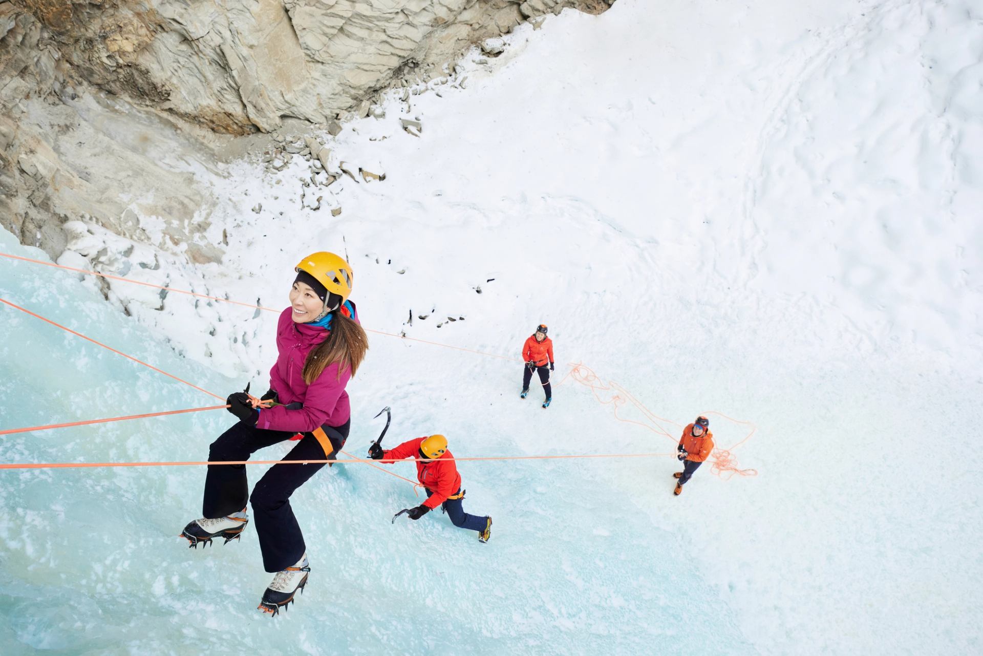 Two ice climbers scale an ice wall in Nordegg, supported by two people at the base.