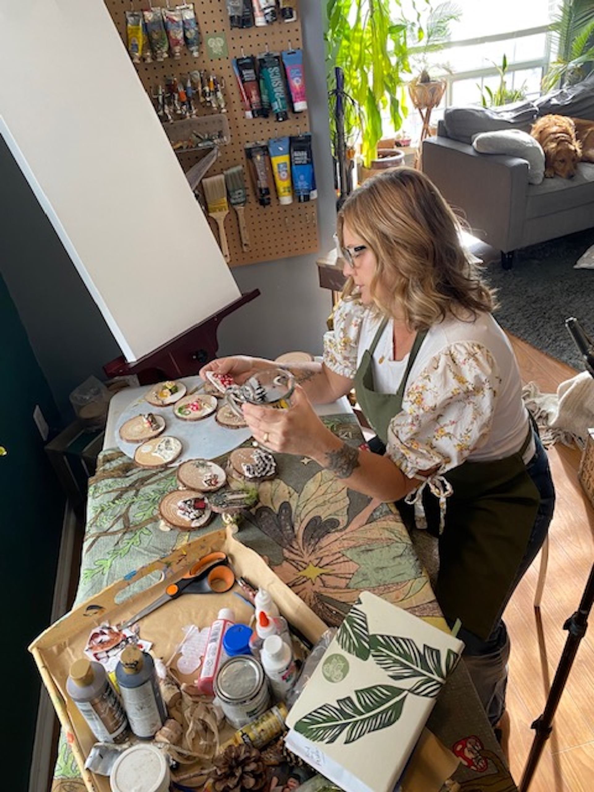 Person painting wooden discs at a table filled with art supplies in a cozy workshop.