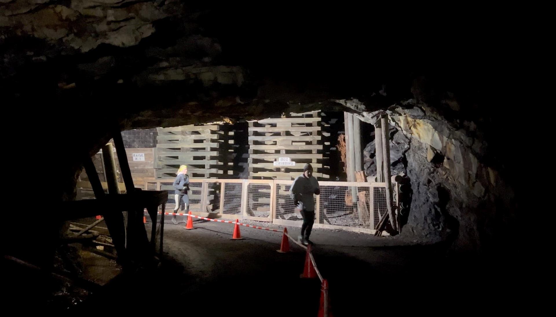Participants walk past wooden supports inside a dark underground cave.
