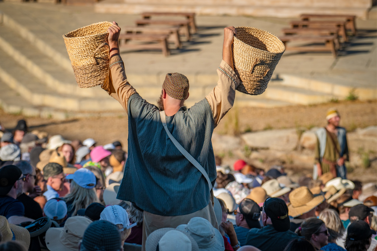 An actor dressed in costume holds up baskets while walking through the audience.