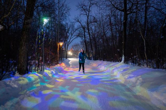 A woman skates down a trail lit with colourful lights at night.