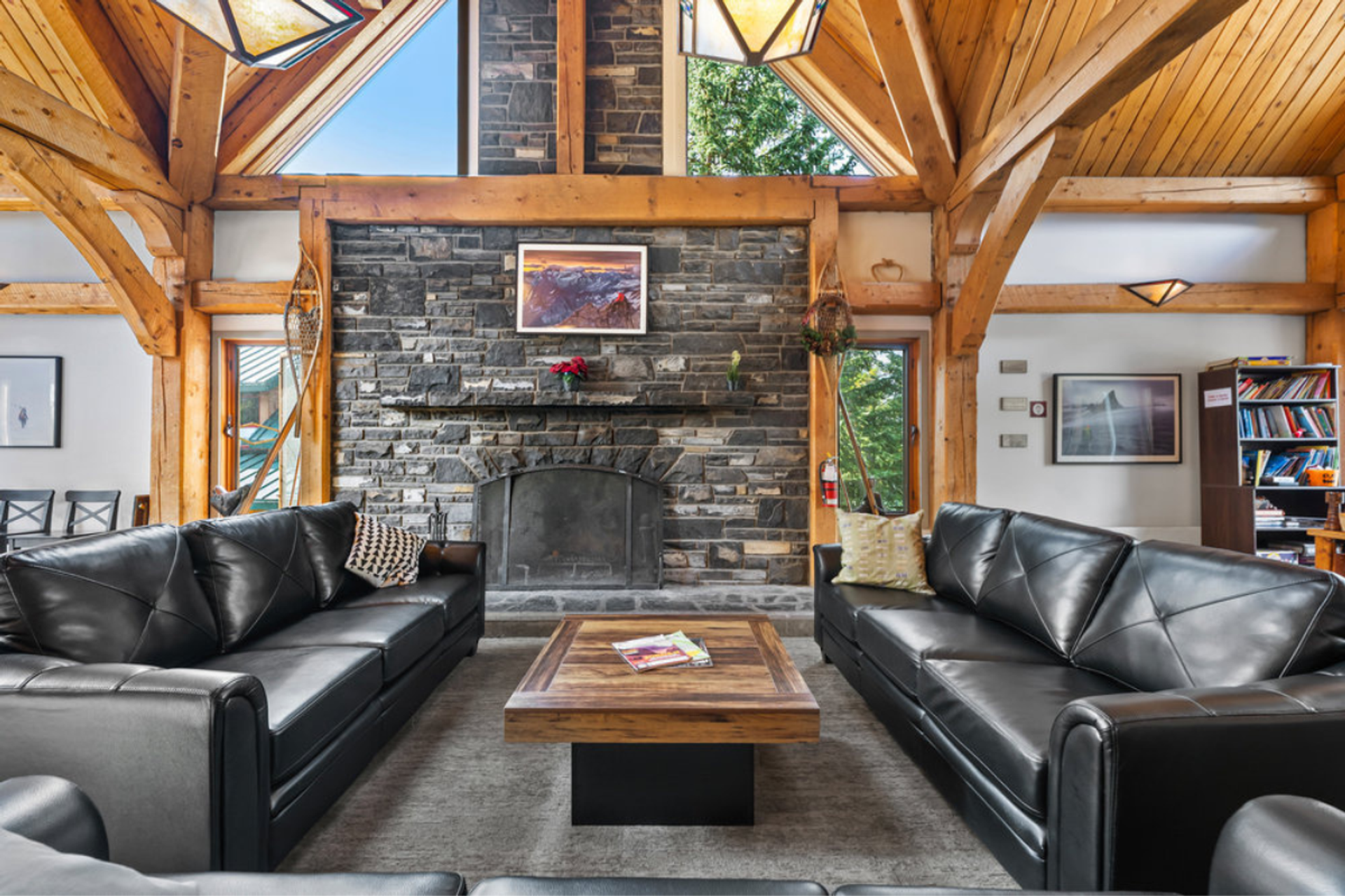 Lounge with dramatic vaulted wooden ceiling, stone fireplace, and black leather sofas.