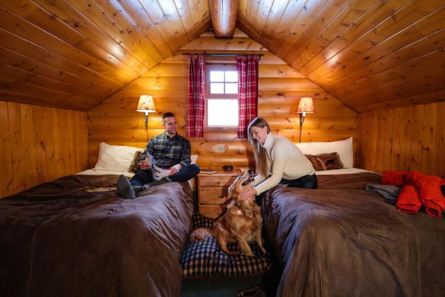 Couple with a dog reading on the bed inside a log cabin at the Baker Creek Mountain Resort