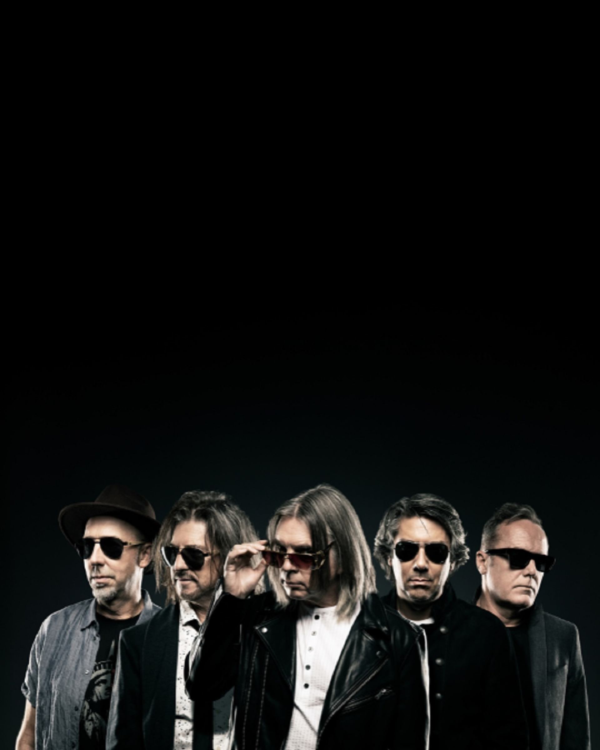 Five people wearing sunglasses and dark clothing stand in a row against black background.