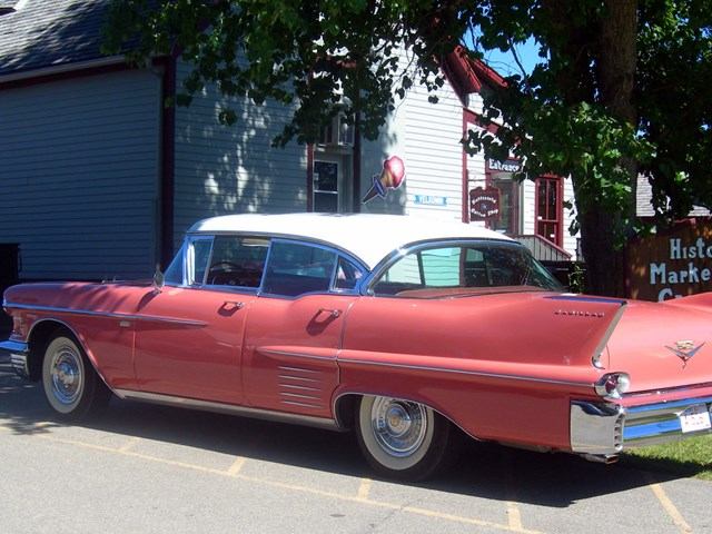 Vintage red and white car parked near trees and building in Historic Markerville.