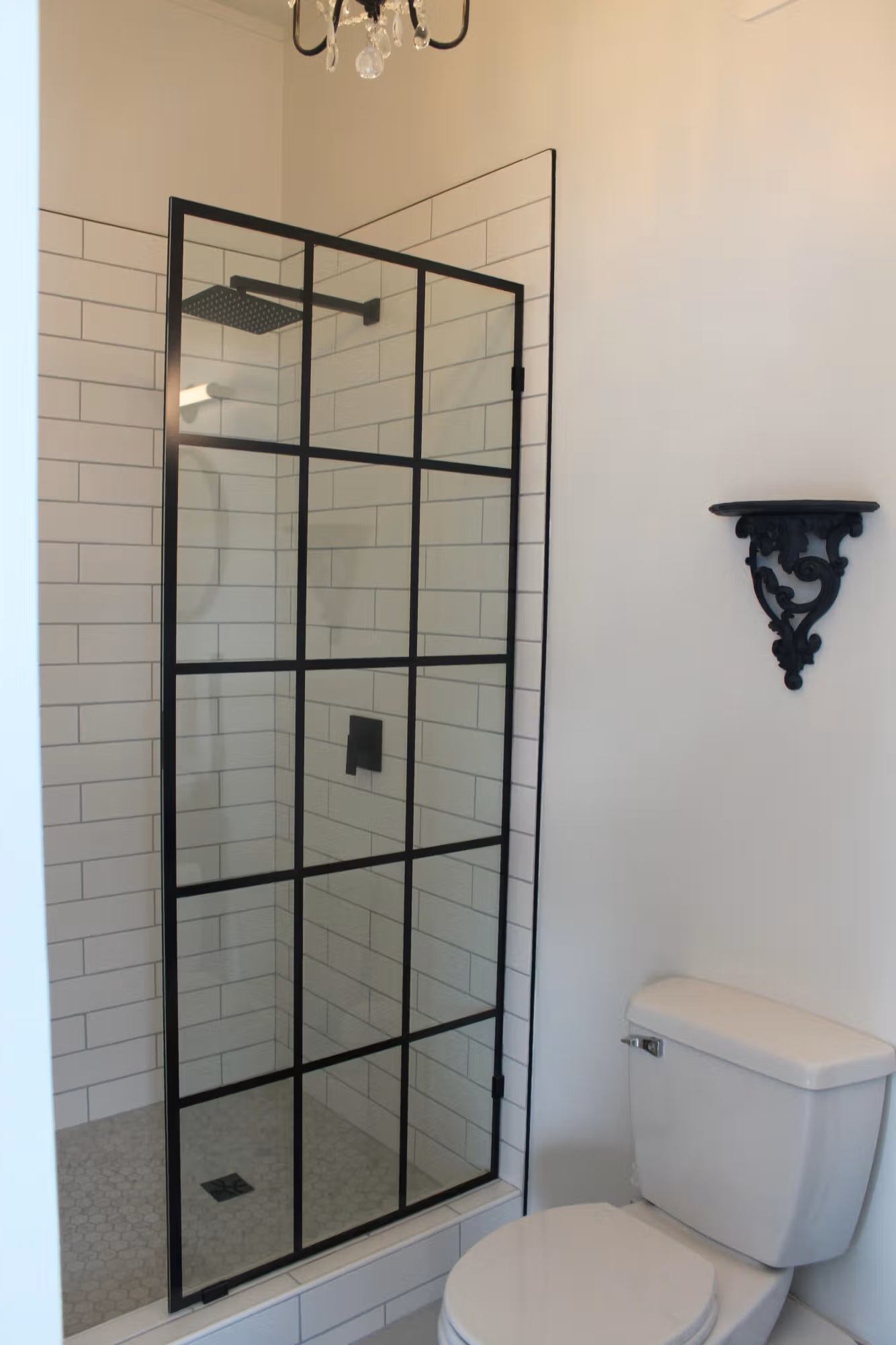Bathroom with glass shower enclosure, subway tile walls, toilet and decorative wall shelf.
