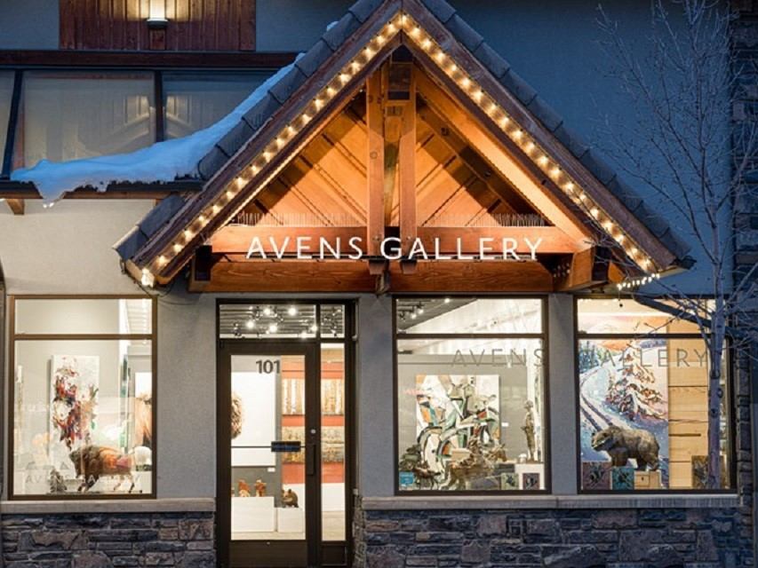 Exterior of Avens Gallery with lit wooden awning and artwork displayed in the front windows.