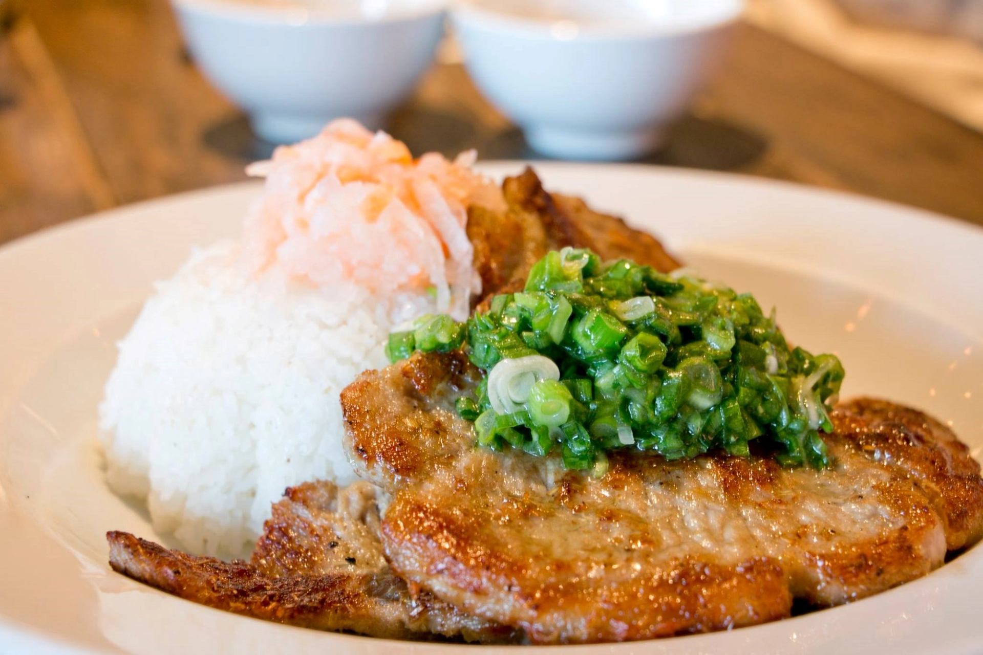Plate of pork chops topped with green onions and sauerkraut, with a white bun.