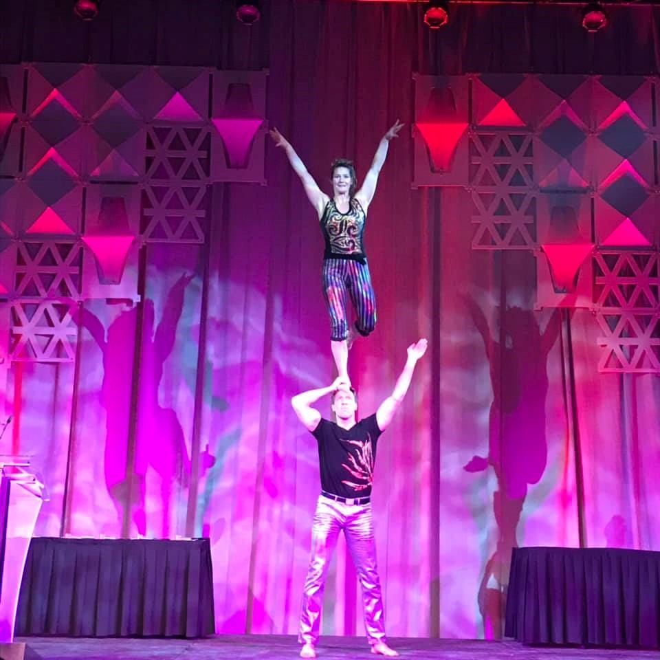 Circus performers pose on stage under purple lights with fog and curtain backdrop.