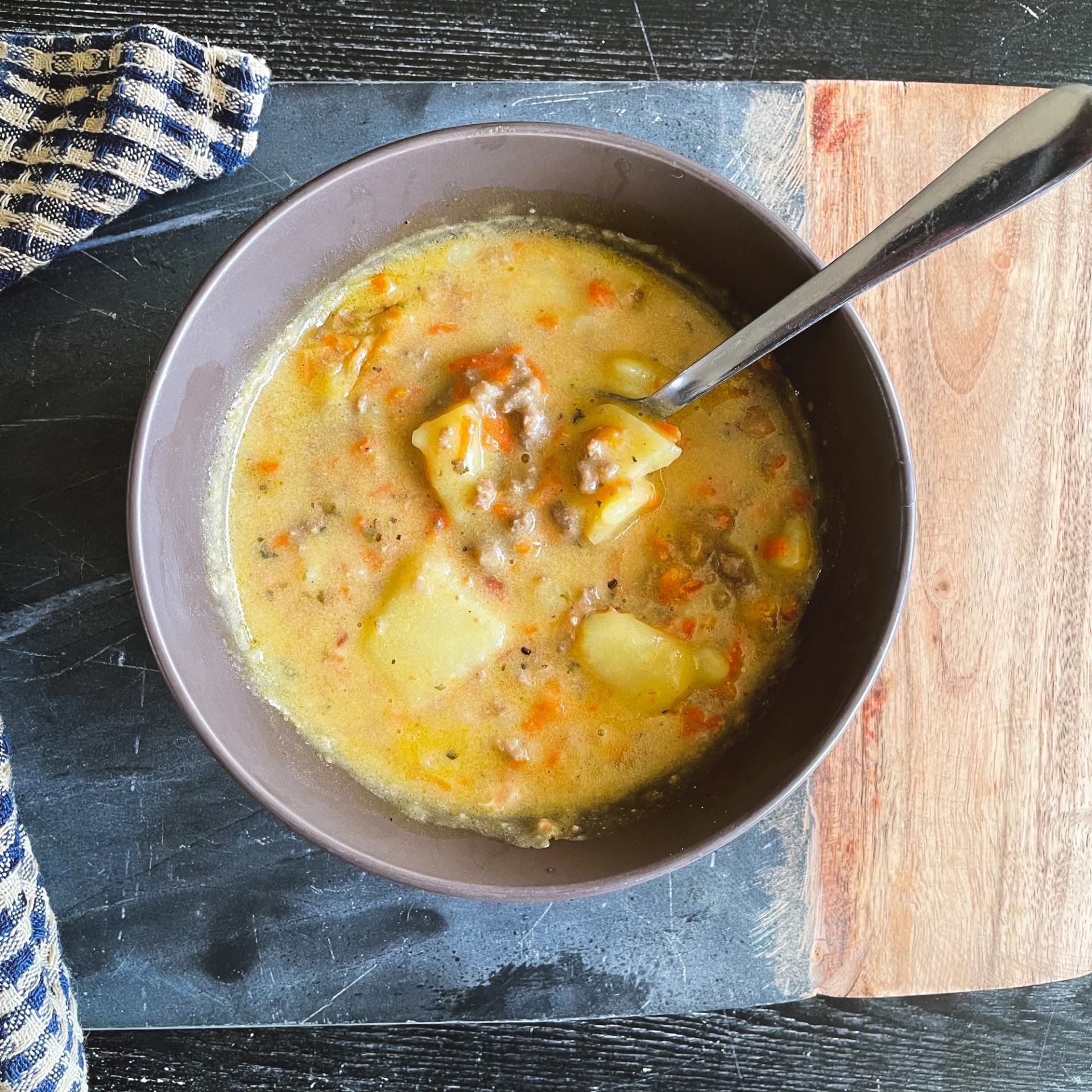 Bowl of creamy potato and ground meat soup with carrots on a wooden board.
