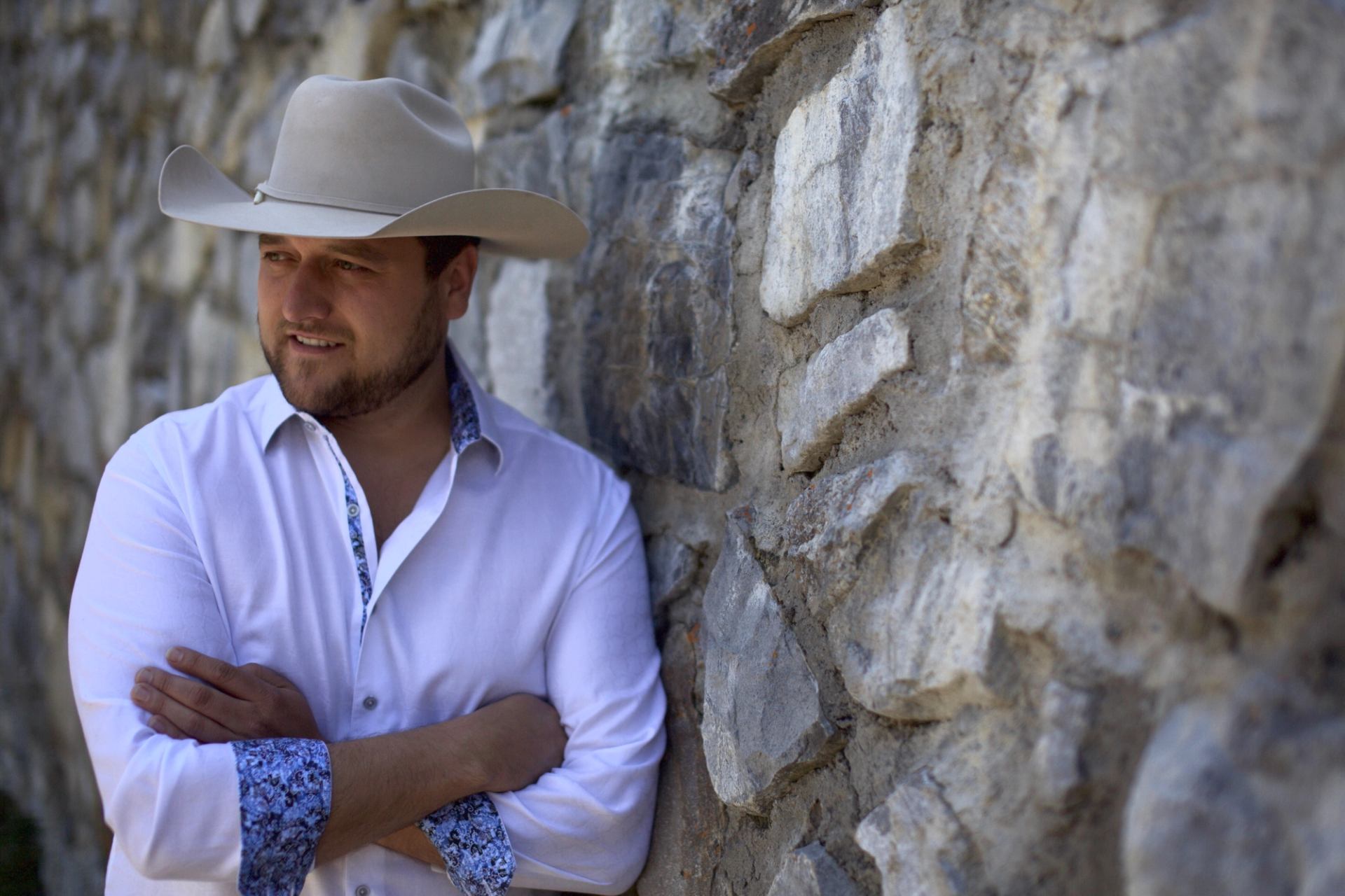 Trevor Panczak leaning against a rock wall wearing a cowboy hat.