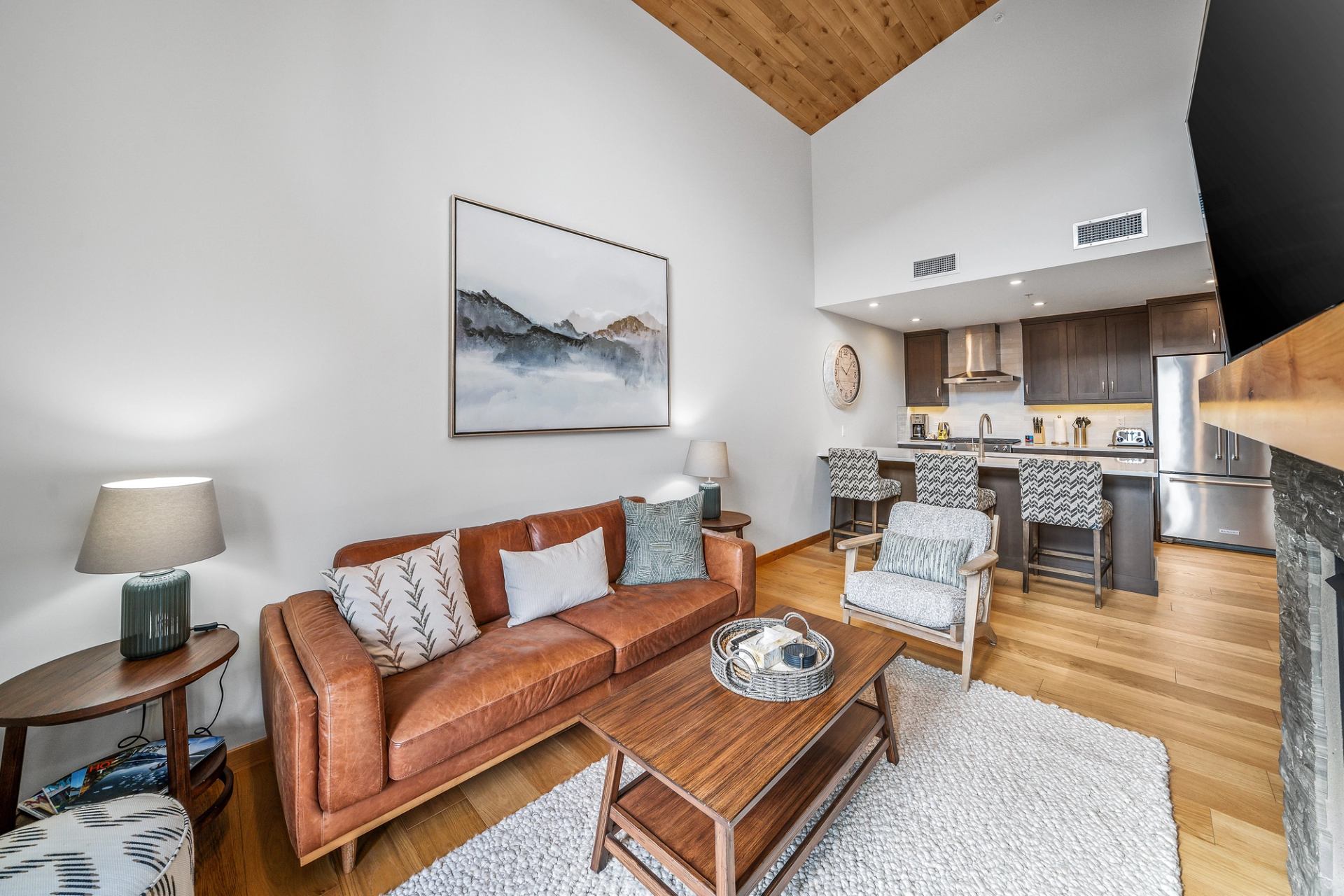Modern open-concept living room with leather sofa, wood accents and kitchen island seating.