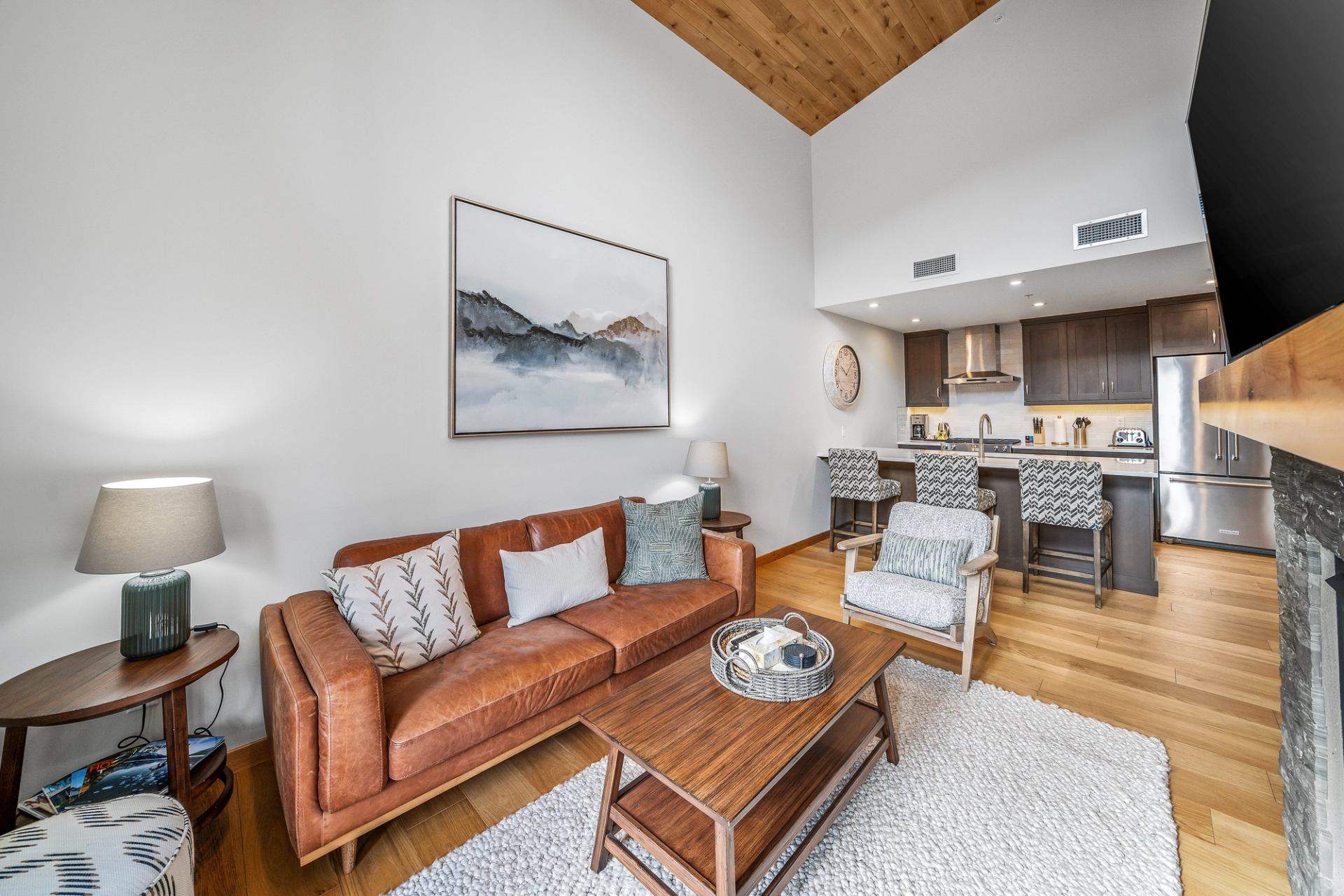 Modern open-concept living room with leather sofa, wood accents and kitchen island seating.