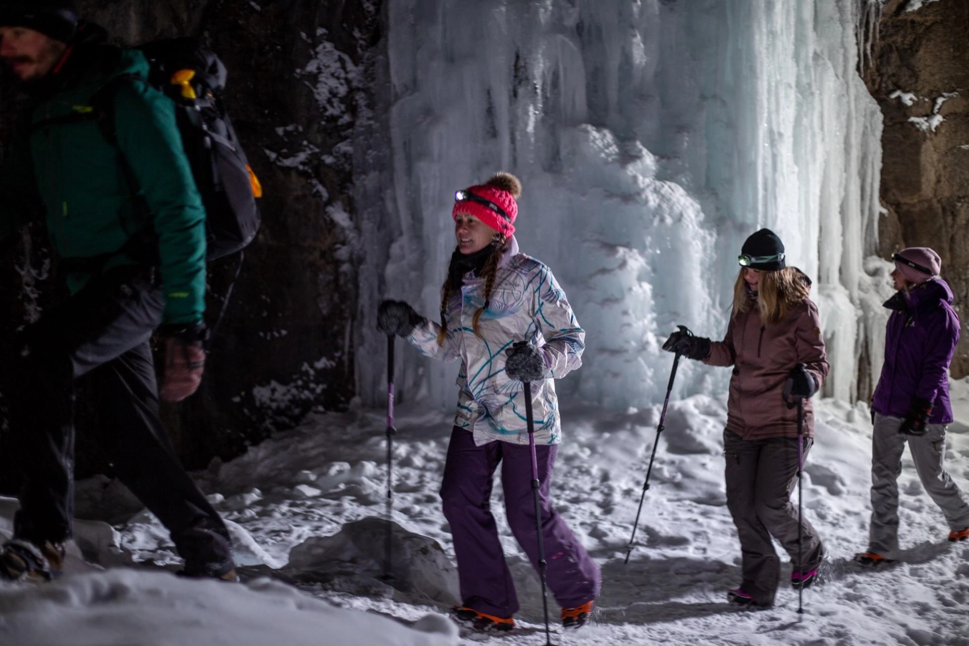 People hiking on snowy terrain near large frozen waterfalls and rocky cliffs in daylight