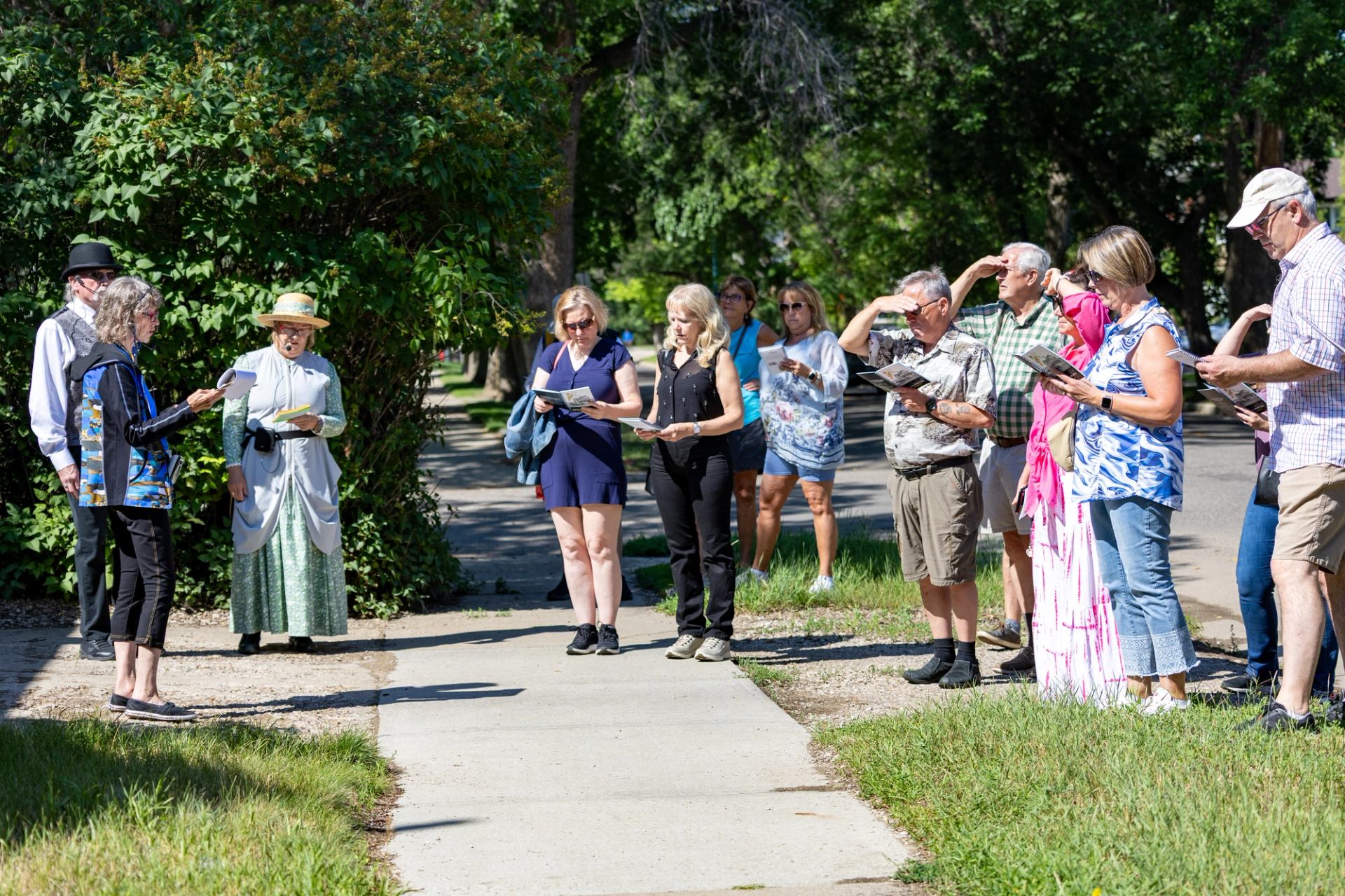 Group of people on sidewalk listening to guide in historic-style clothing outdoors.