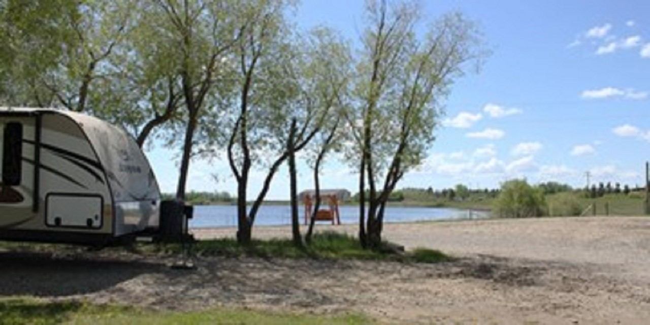 Recreational vehicle parked at riverside campground, with trees and open shoreline visible.