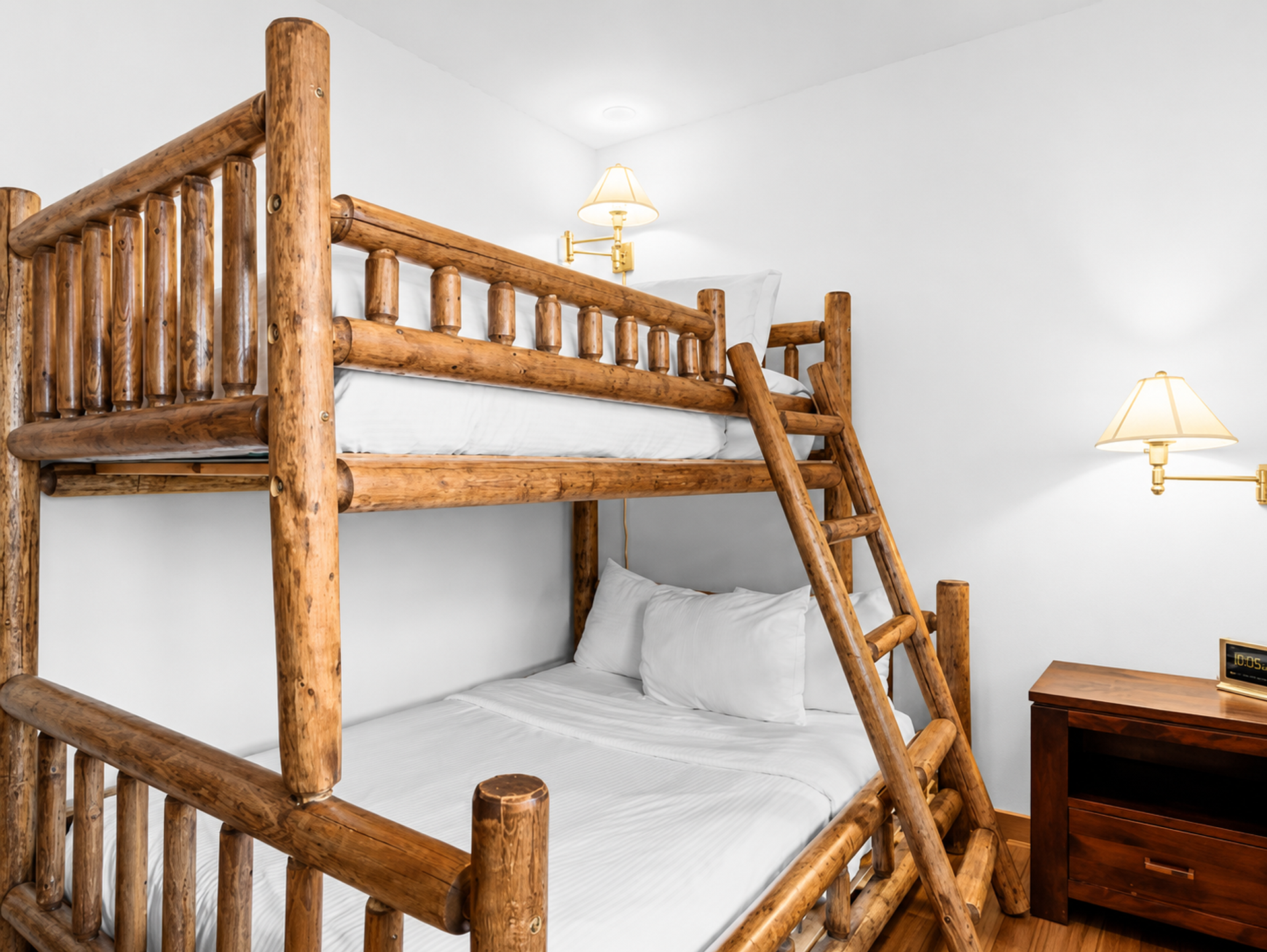 Wooden bunk bed with white bedding beside nightstand and wall-mounted lamps.