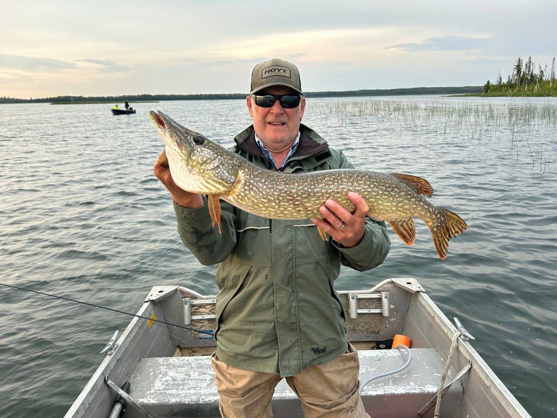 Person standing in a boat holding a large fish above the water.