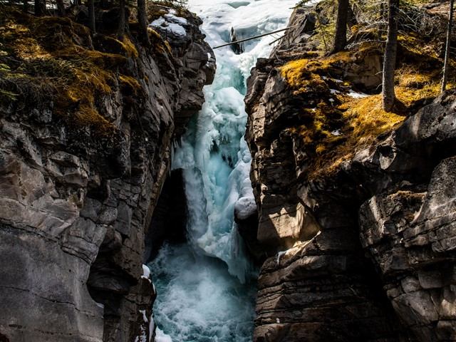 Waterfall pouring between rocky cliffs with forest trees and mossy green rocks.