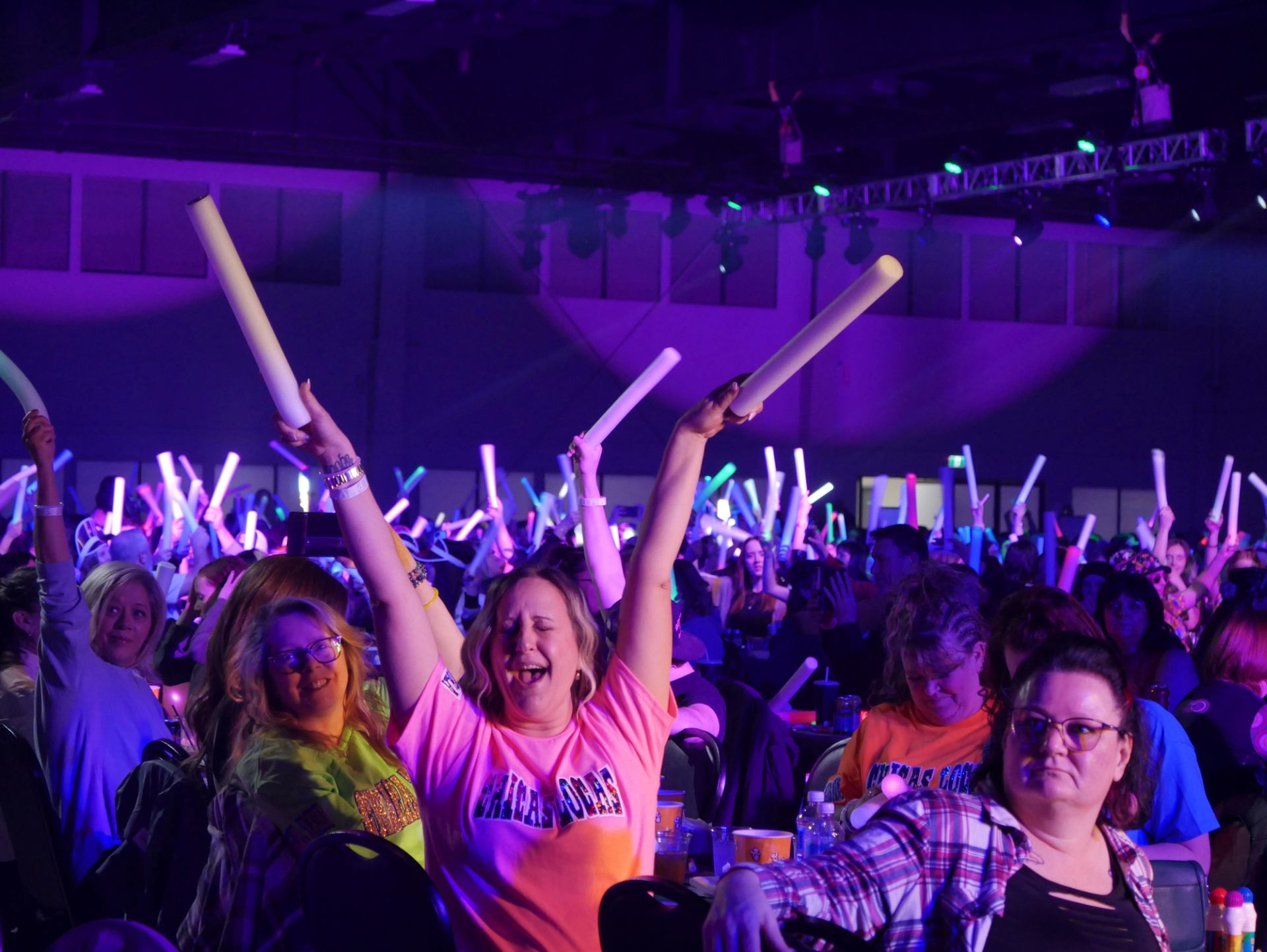 Excited crowd holding light sticks under purple stage lighting.