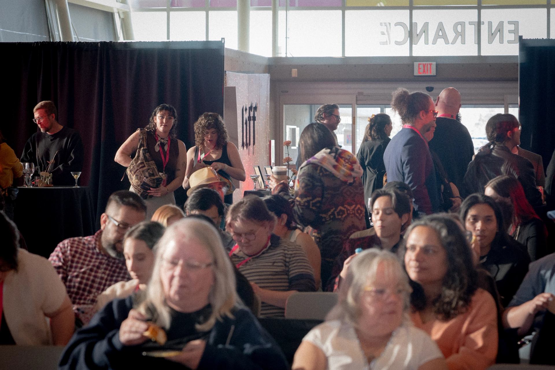 Audience members sit and stand in a busy indoor event entrance area.