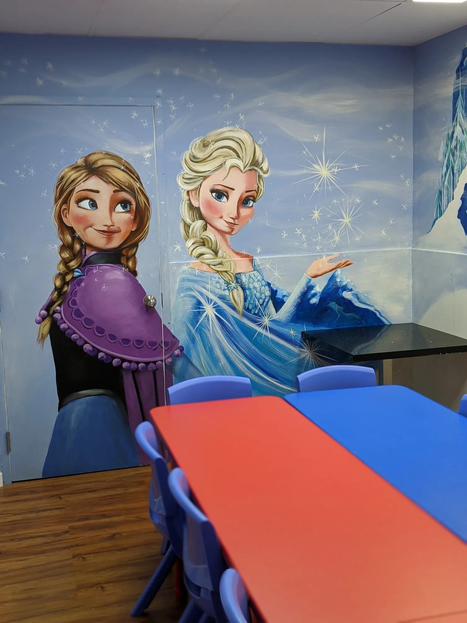 Classroom with Frozen wall mural behind red and blue tables and plastic chairs.