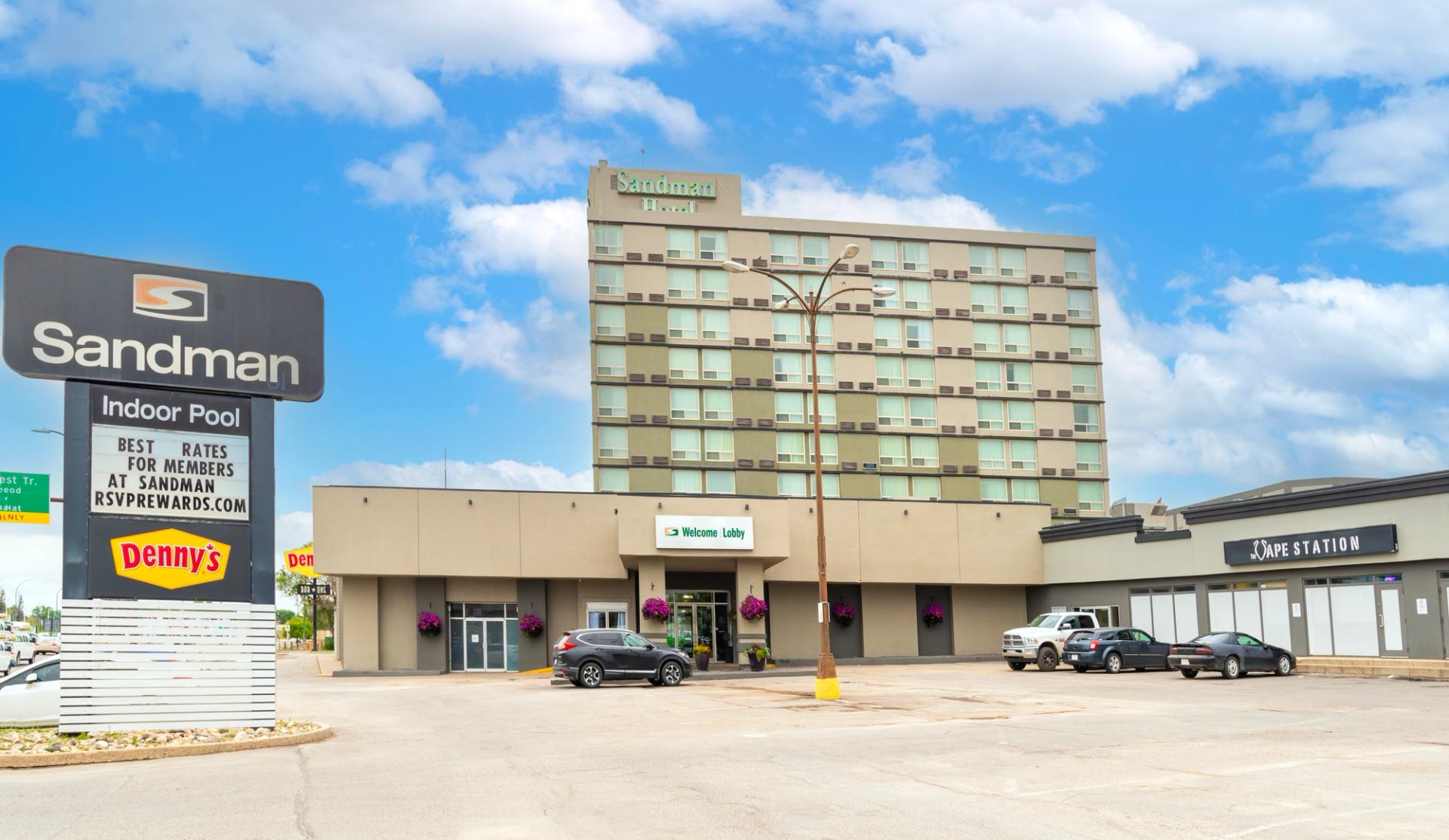 Exterior view of Sandman Hotel Lethbridge with parking, signage, and nearby businesses.
