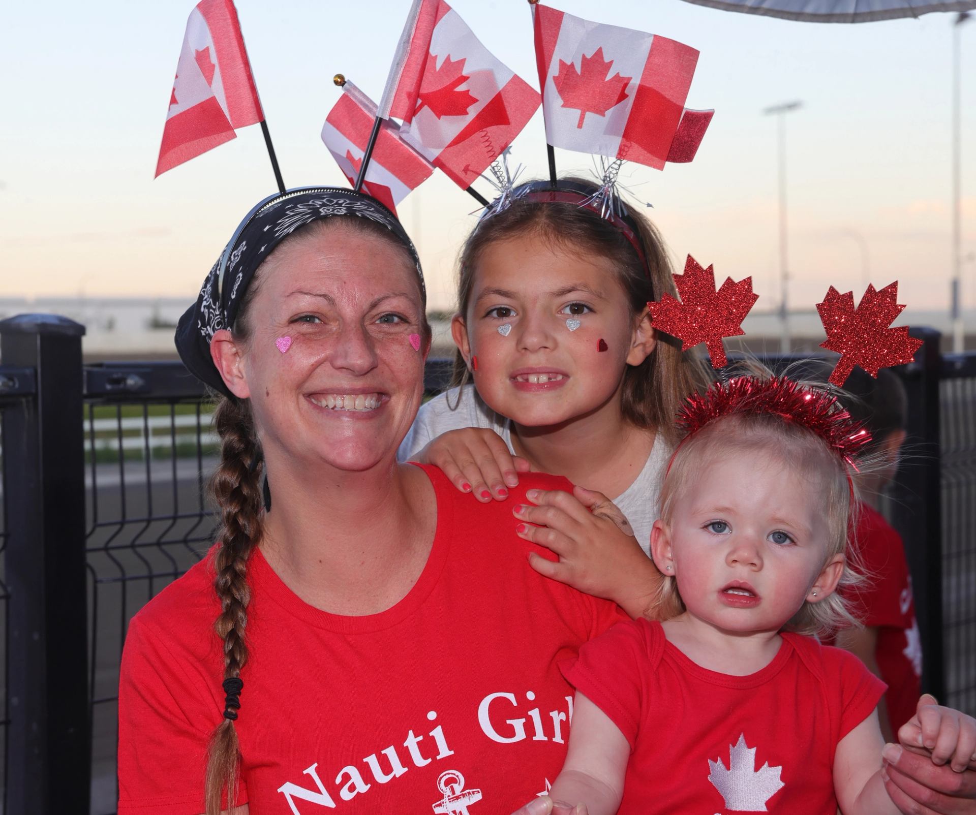 Group wearing red shirts and Canadian flag headbands during Canada Day festivities at a racetrack.