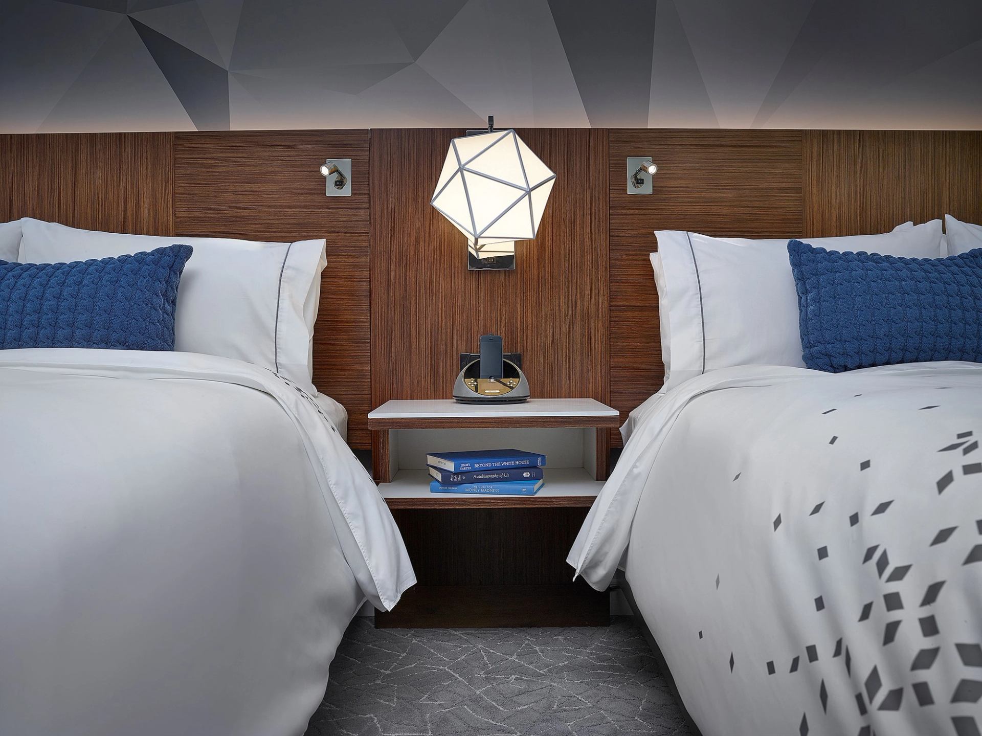 Sleek hotel room with twin beds, blue accents, and modern lighting.